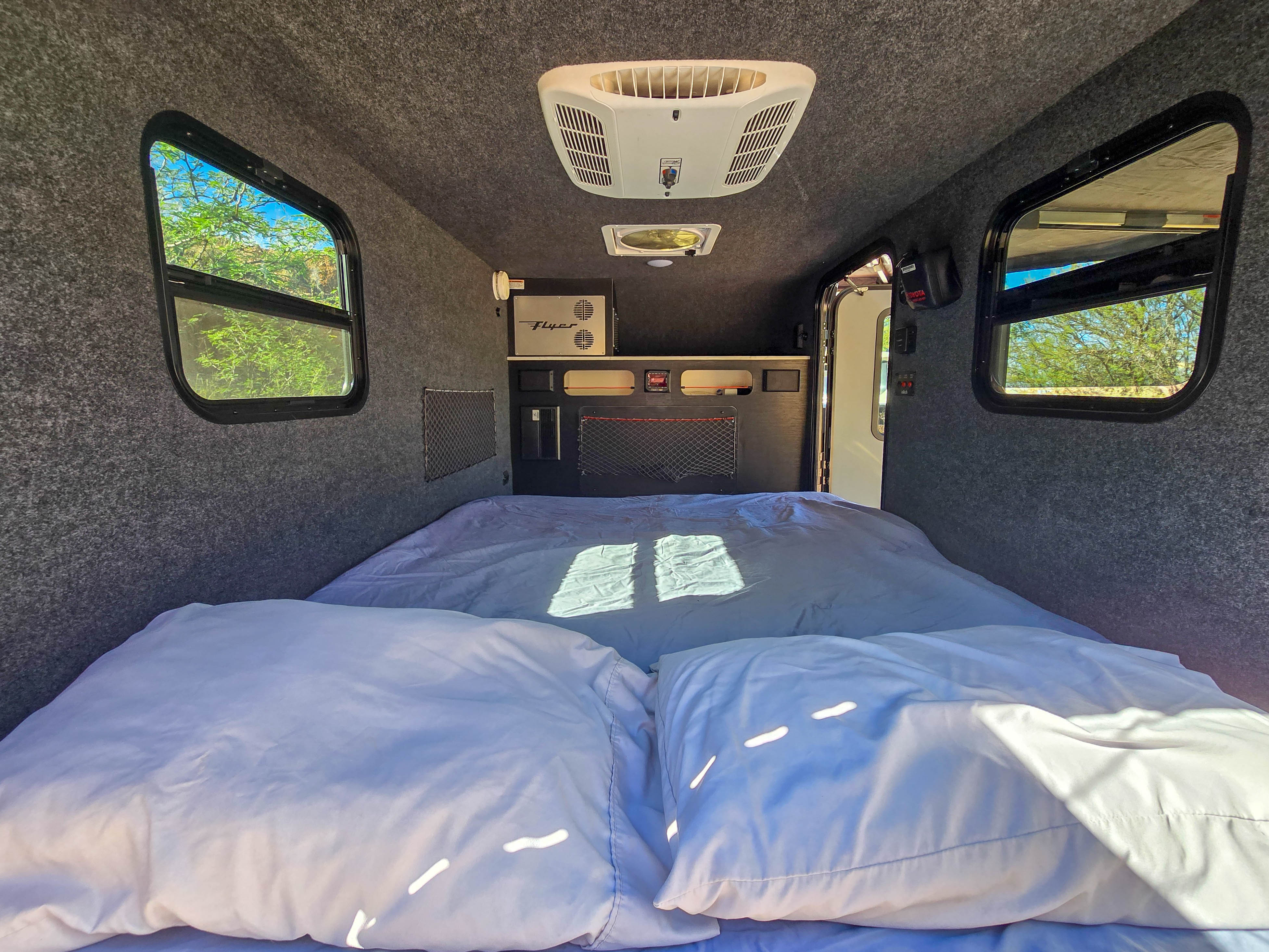 Cozy RV rental interior with a comfy bed, windows, and built-in features for your next camping adventure.. InTech RV Flyer 2024
