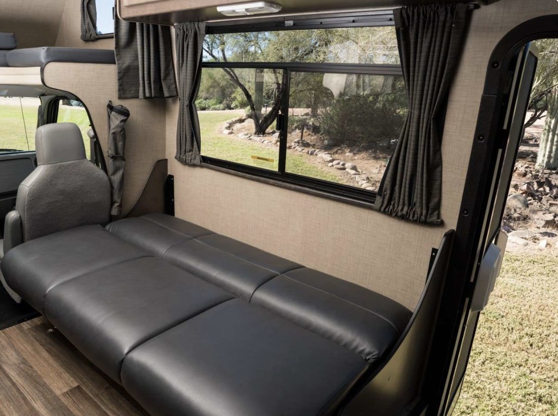 Spacious RV rental interior with a comfy black sleeper sofa, large window views, and driver's seat visible. Perfect for road trips.. Thor Majestic 2019