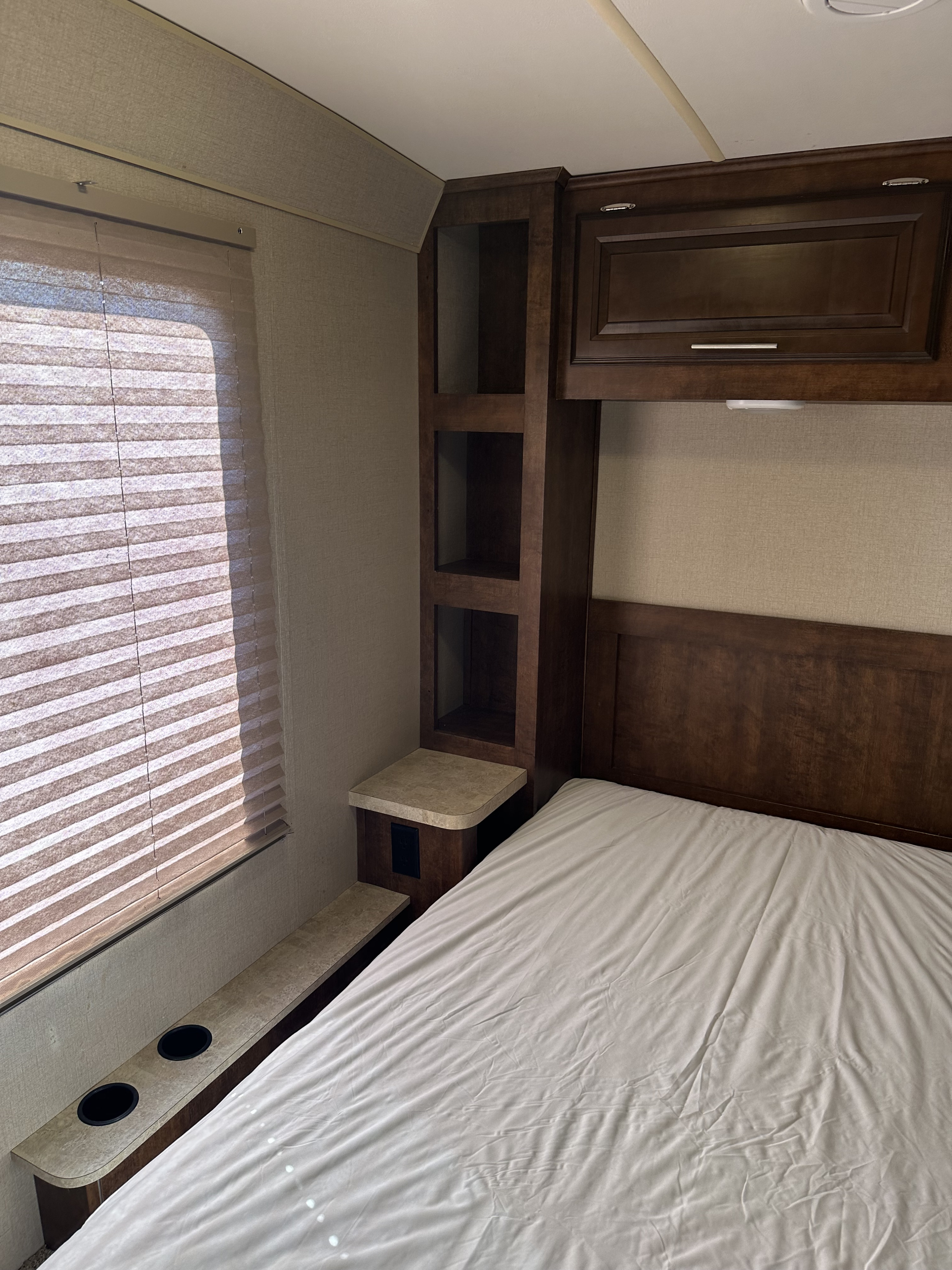 This RV rental bedroom features a comfortable bed, overhead cabinetry, built-in shelves, and a window with blinds.. Forest River FR3 2017