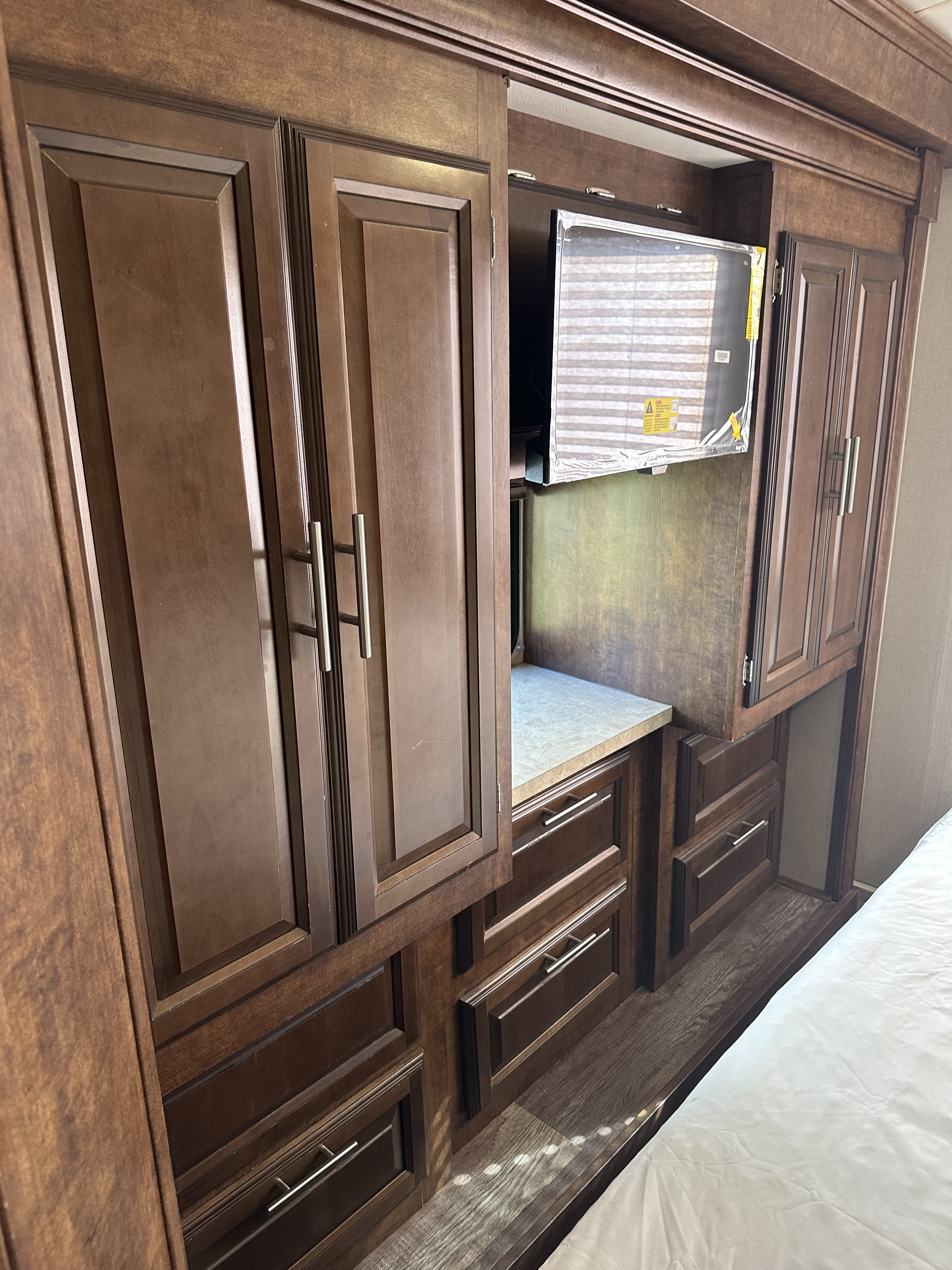 Explore this RV rental's bedroom: dark wood cabinets, drawers, counter, and TV provide ample storage and entertainment.. Forest River FR3 2017
