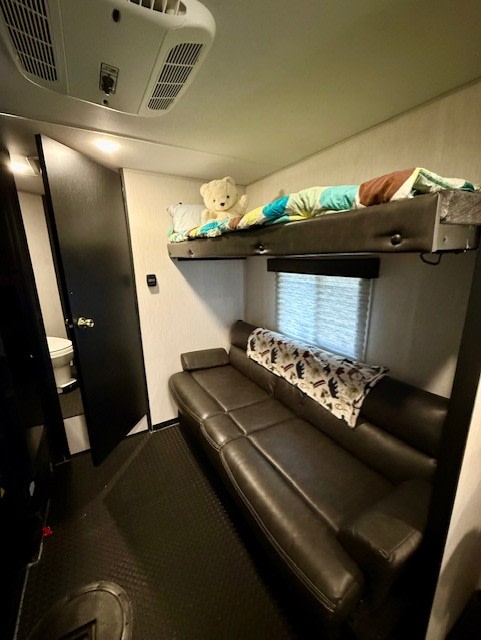 This RV rental interior features bunk beds with a teddy bear, a dark sofa, and a small bathroom visible through an open door.. Forest River Cherokee Grey Wolf Special Edition 2023