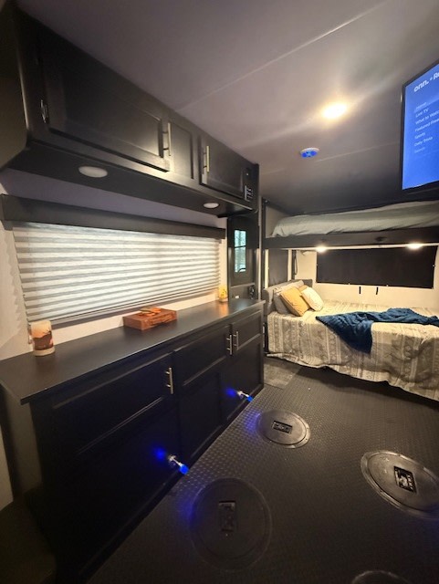 Cozy RV rental interior showcasing dark cabinets, window with blinds, comfortable beds (bunk above), TV, and floor tie-downs.. Forest River Cherokee Grey Wolf Special Edition 2023