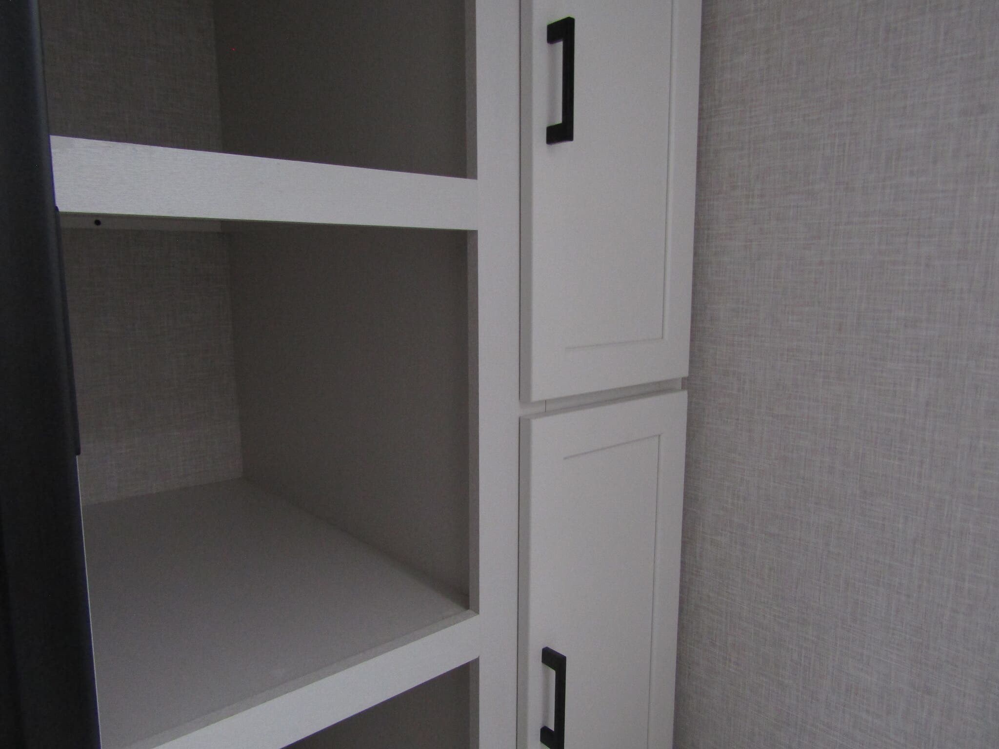 RV rental storage options: White shelves are empty, next to cabinets with black handles and a textured gray wall.. Jayco Jay Flight SLX 2025