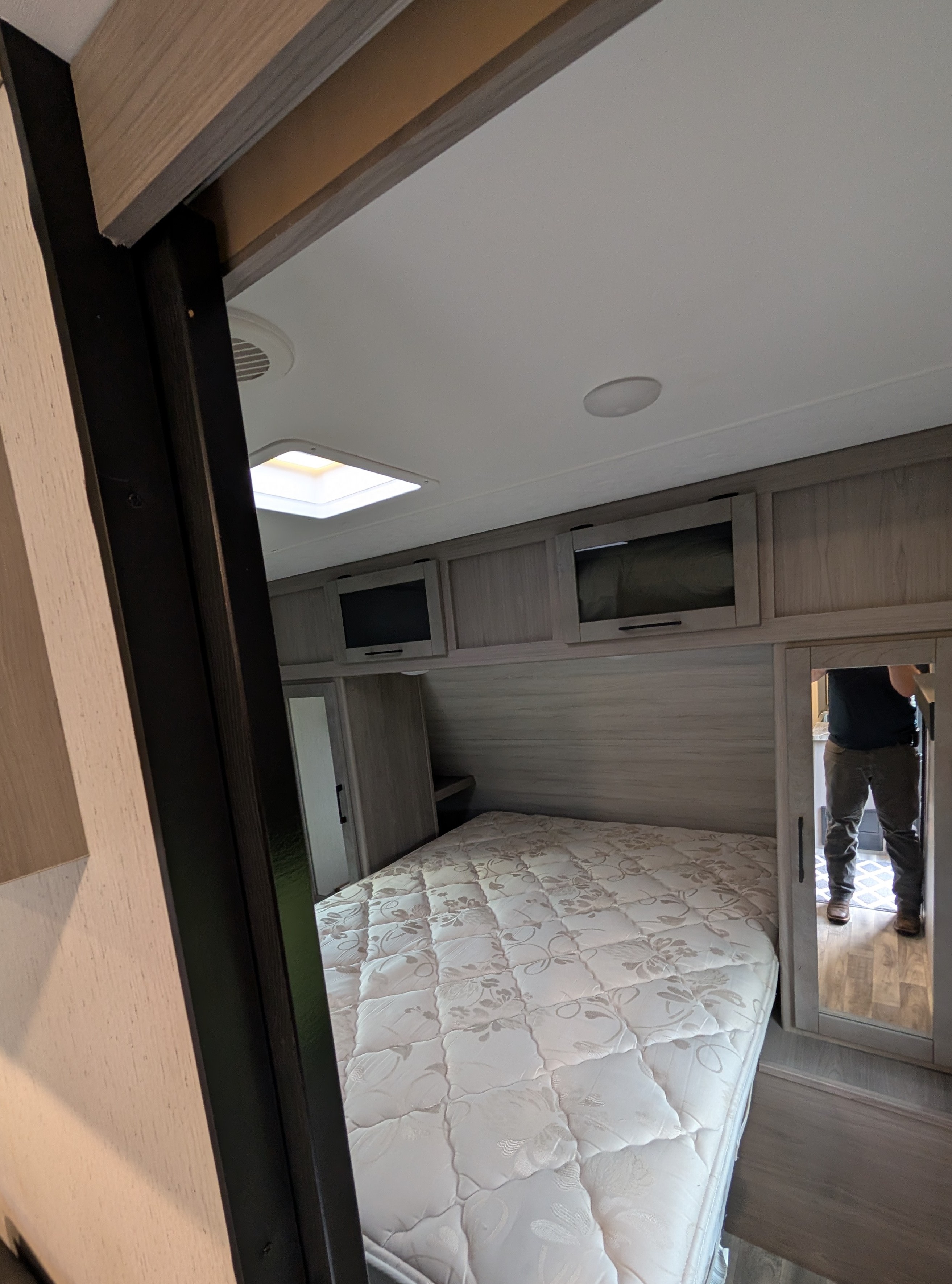 View of an RV rental bedroom with a clean mattress, light wood overhead cabinets, and a mirrored closet reflecting a person.. Dutchmen Kodiak Ultra Lite 2022