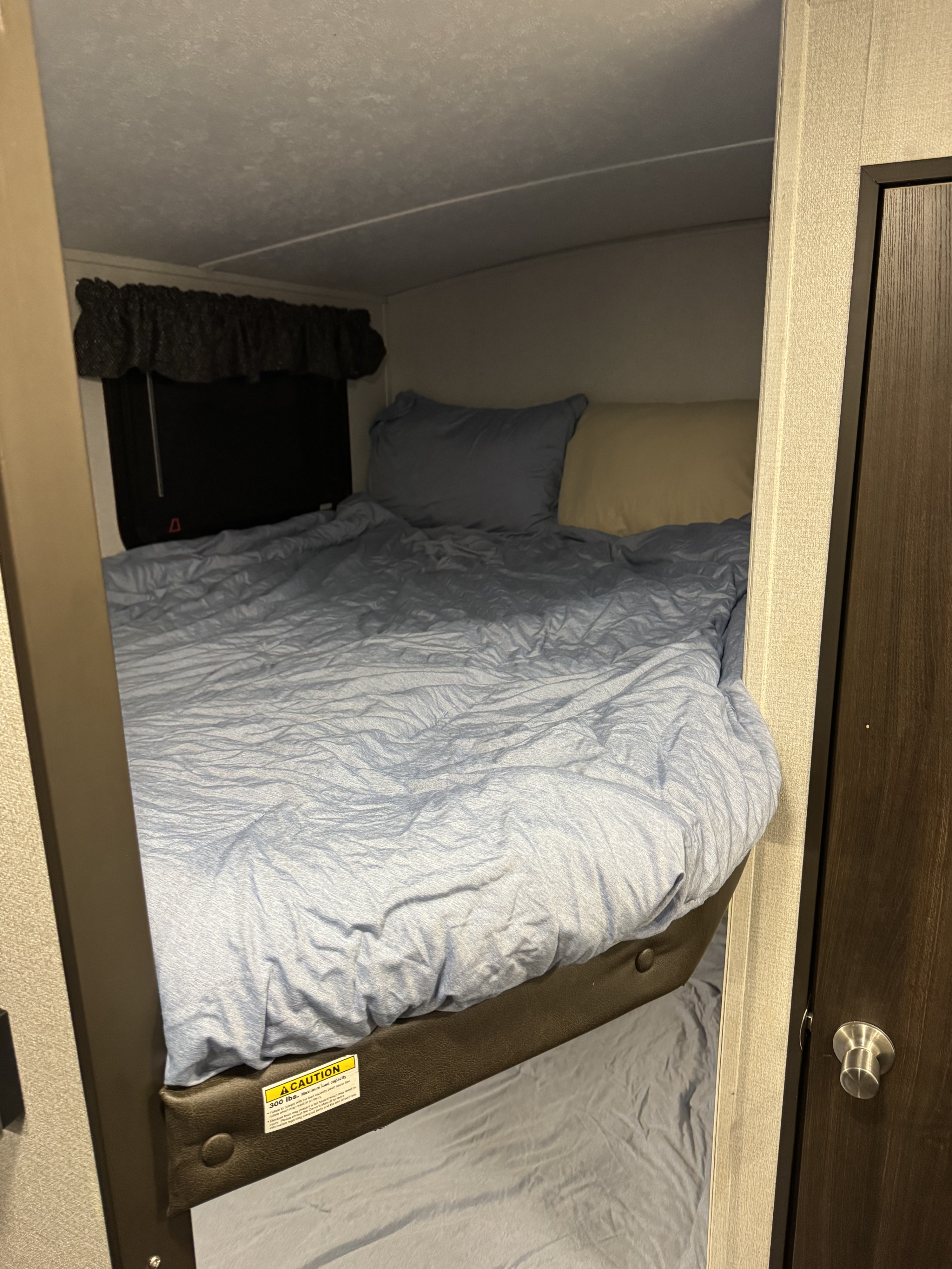 Cozy bunk beds inside an RV rental, featuring blue bedding, pillows, a window, and a 300 lbs warning sticker.. Keystone RV Springdale 2020