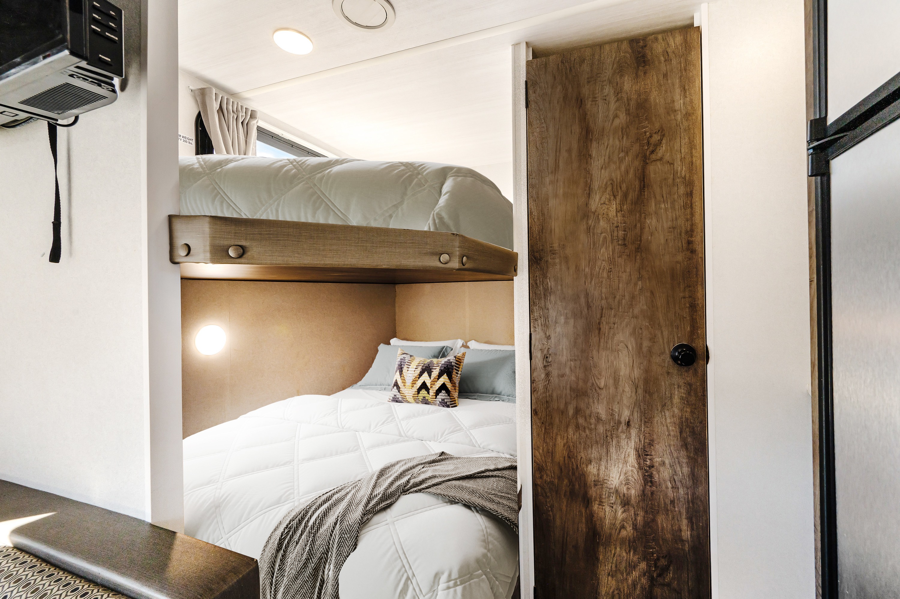 Cozy RV rental interior featuring modern bunk beds, a wall-mounted TV, and wooden accents, perfect for family travel.. Forest River Wildwood X-Lite 2020