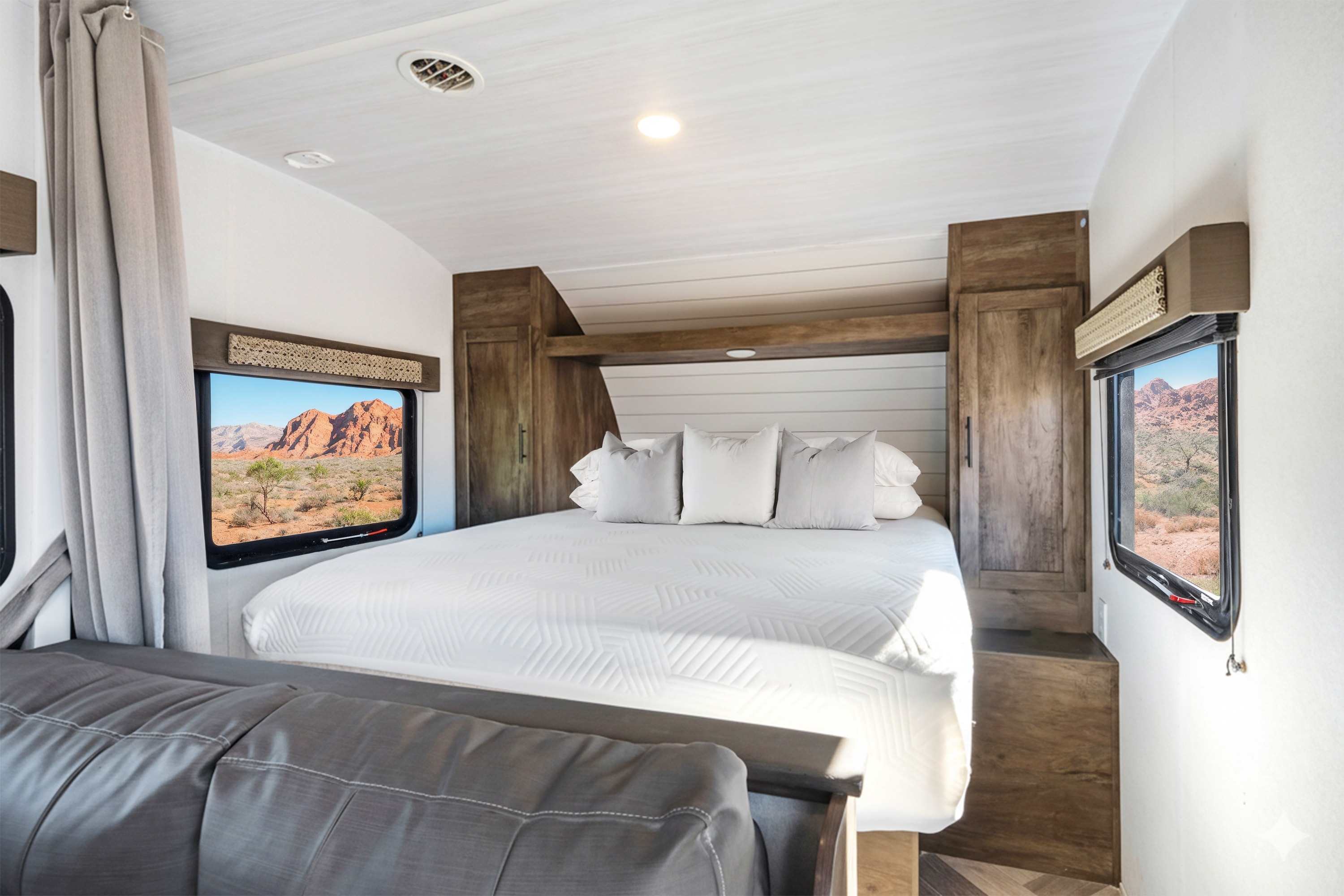 RV rental bedroom features a comfy bed, white linens, wood cabinets, and stunning desert mountain views from two windows.. Forest River Wildwood X-Lite 2020