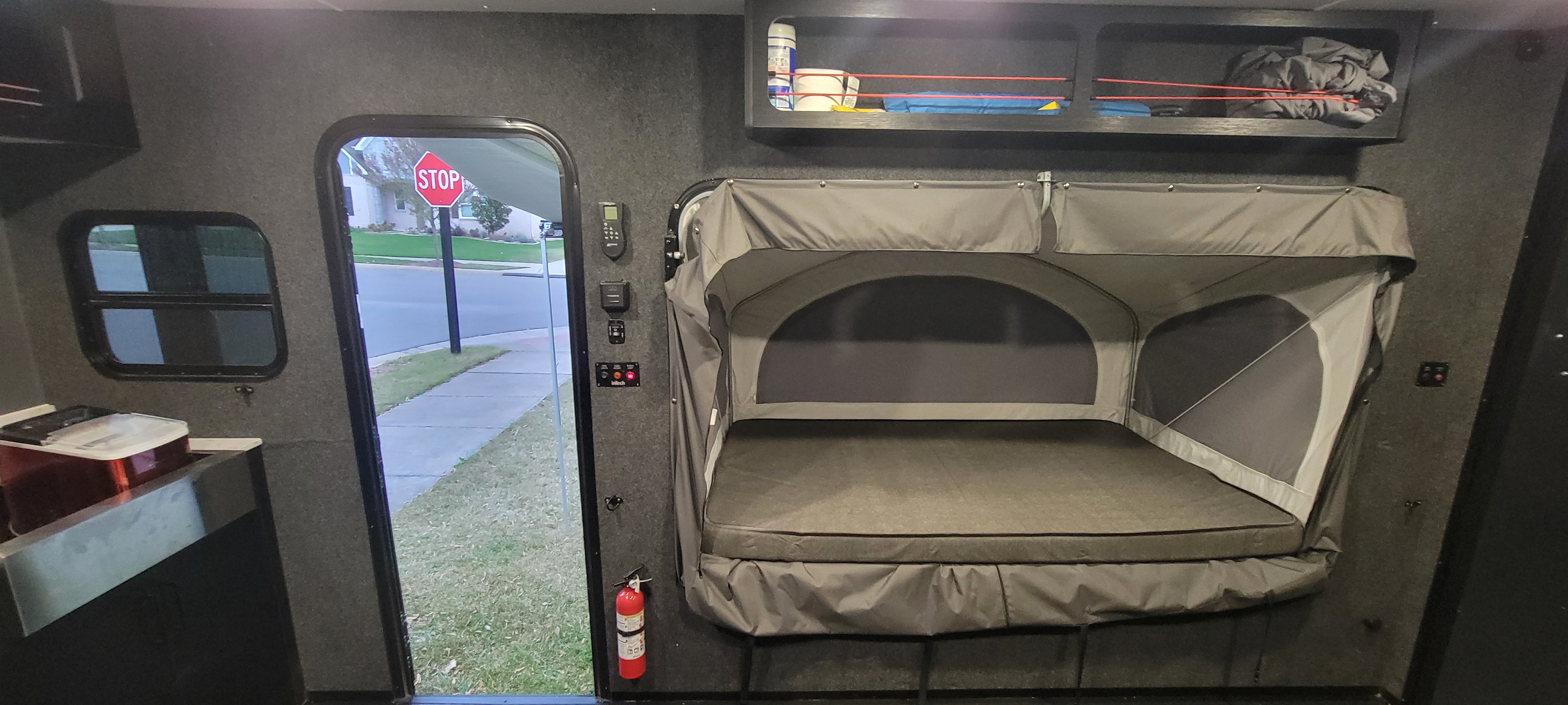 Inside an rv rental: a pop-up bed, controls, window & open door looking at a stop sign on a residential street.. InTech RV Flyer Discover 2024