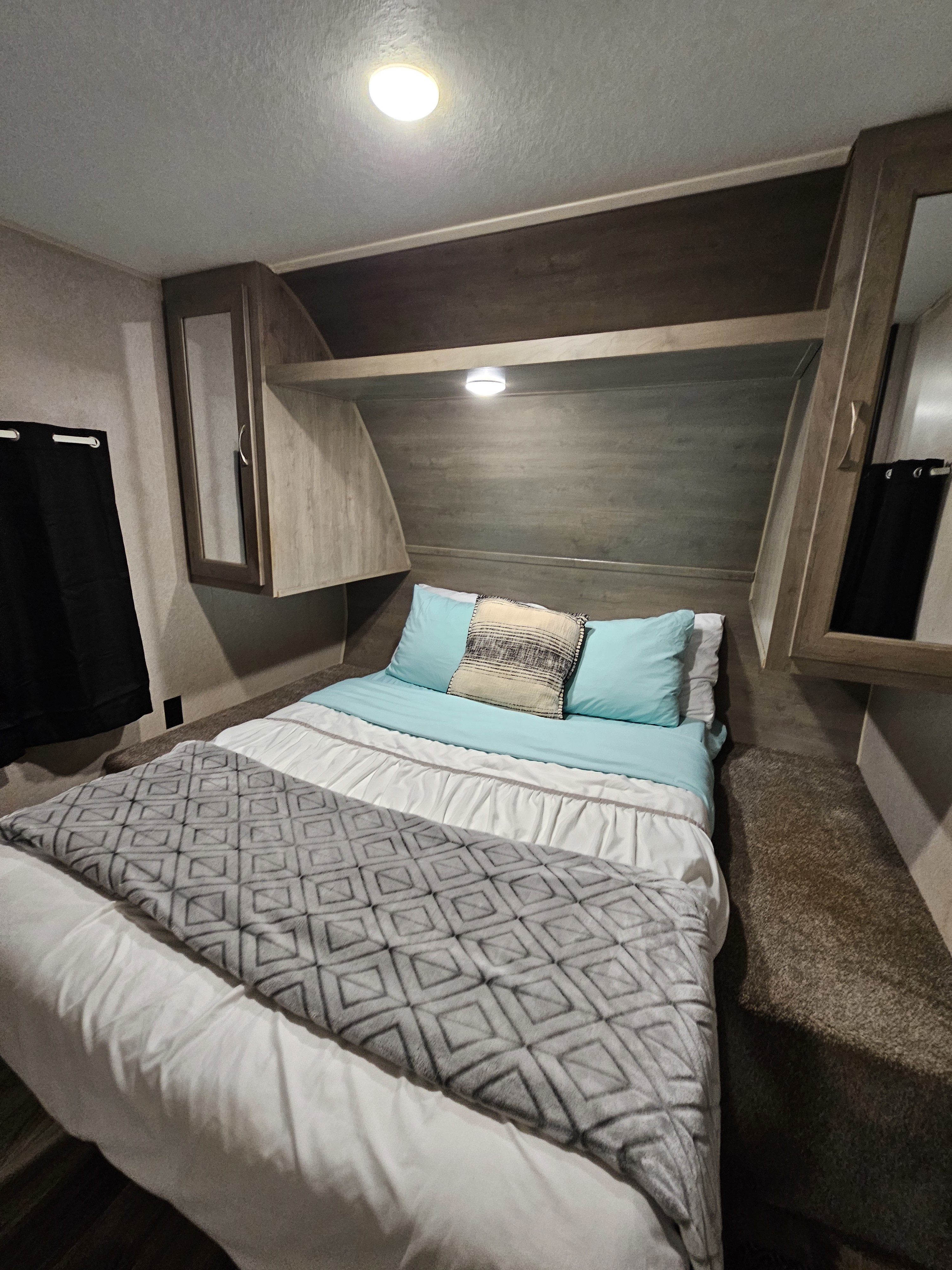 Cozy RV rental bedroom with light blue bedding, overhead cabinets, and soft lighting for your journey.. Forest River Palomino Puma XLE 2019