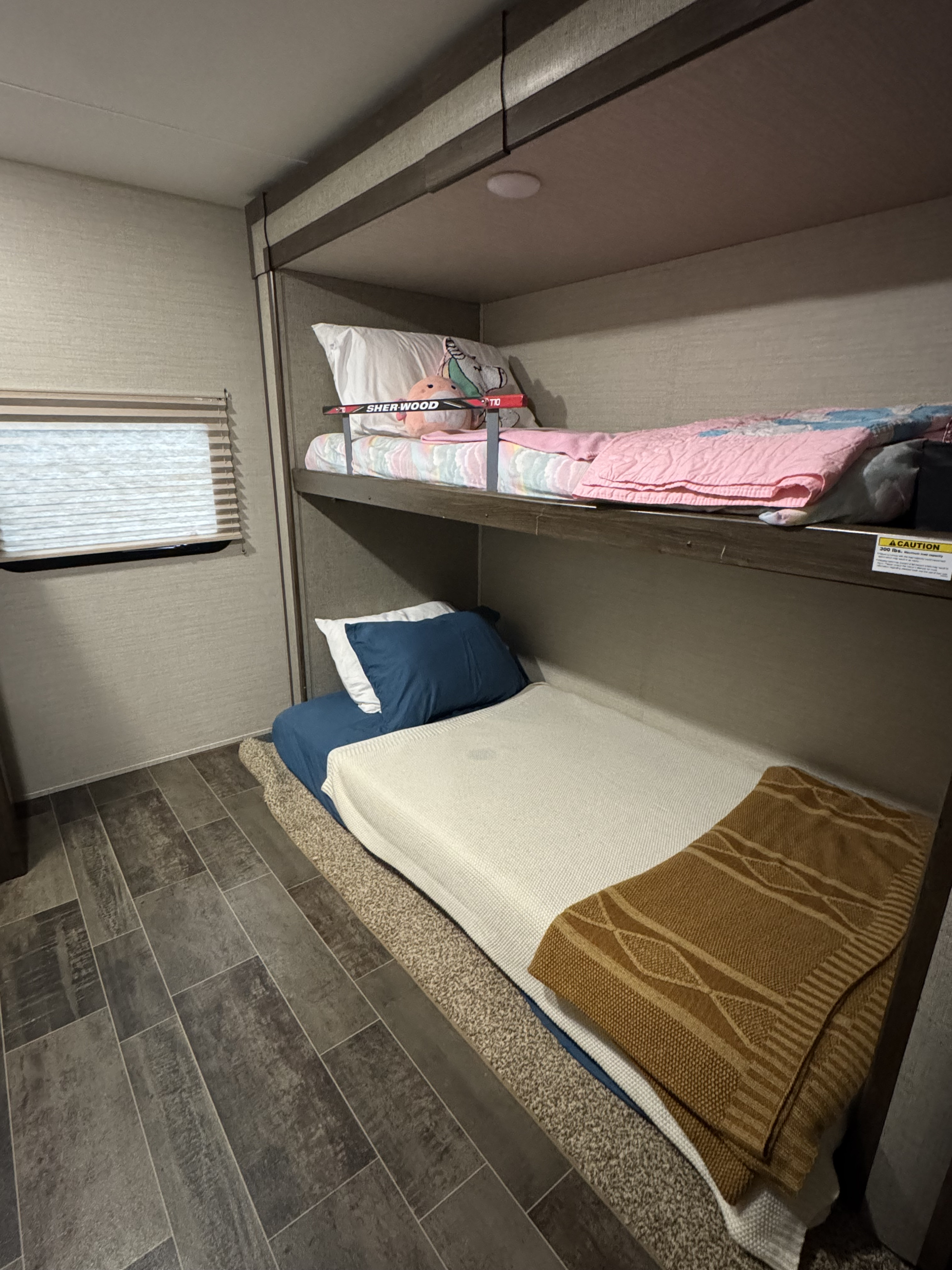 Inside an RV rental, a bunk bed setup with cozy bedding and safety rail. Features window blinds and compact flooring.. Keystone RV Bullet Ultra Lite 2019