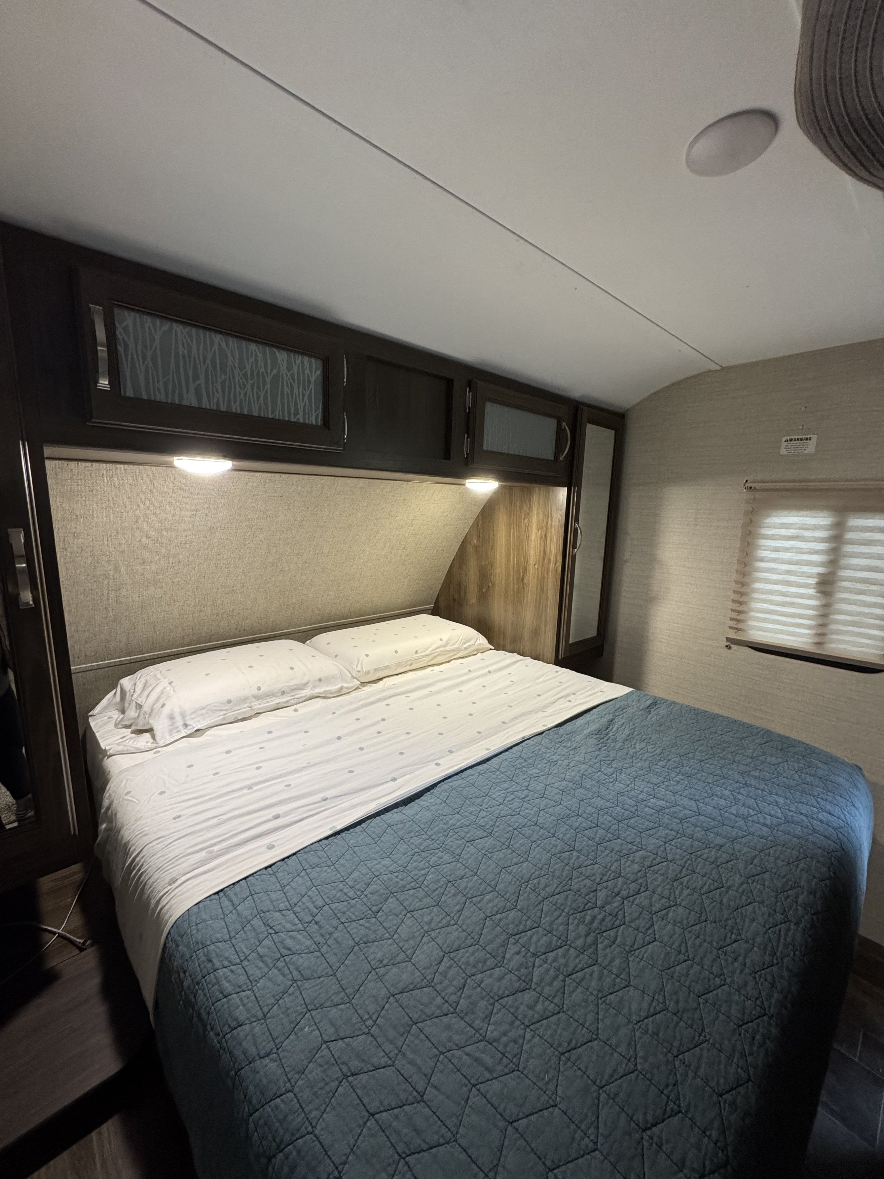 Cozy RV rental bedroom with a comfy bed, blue quilted spread, overhead storage cabinets, and warm ambient lighting for a relaxing stay.. Keystone RV Bullet Ultra Lite 2019