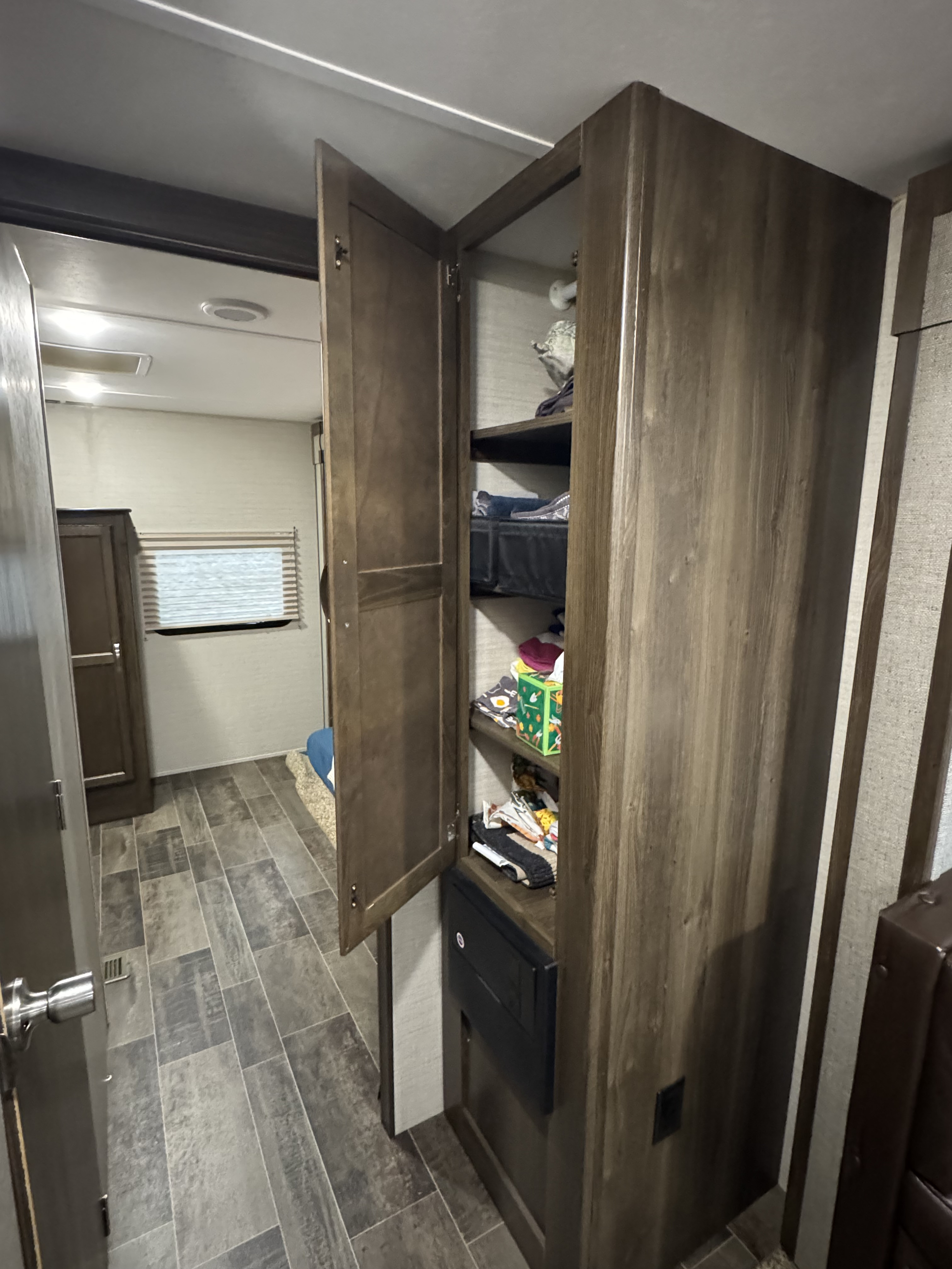 This RV rental interior features an open wooden storage cabinet revealing shelves with items, alongside a hallway leading to a rear room.. Keystone RV Bullet Ultra Lite 2019