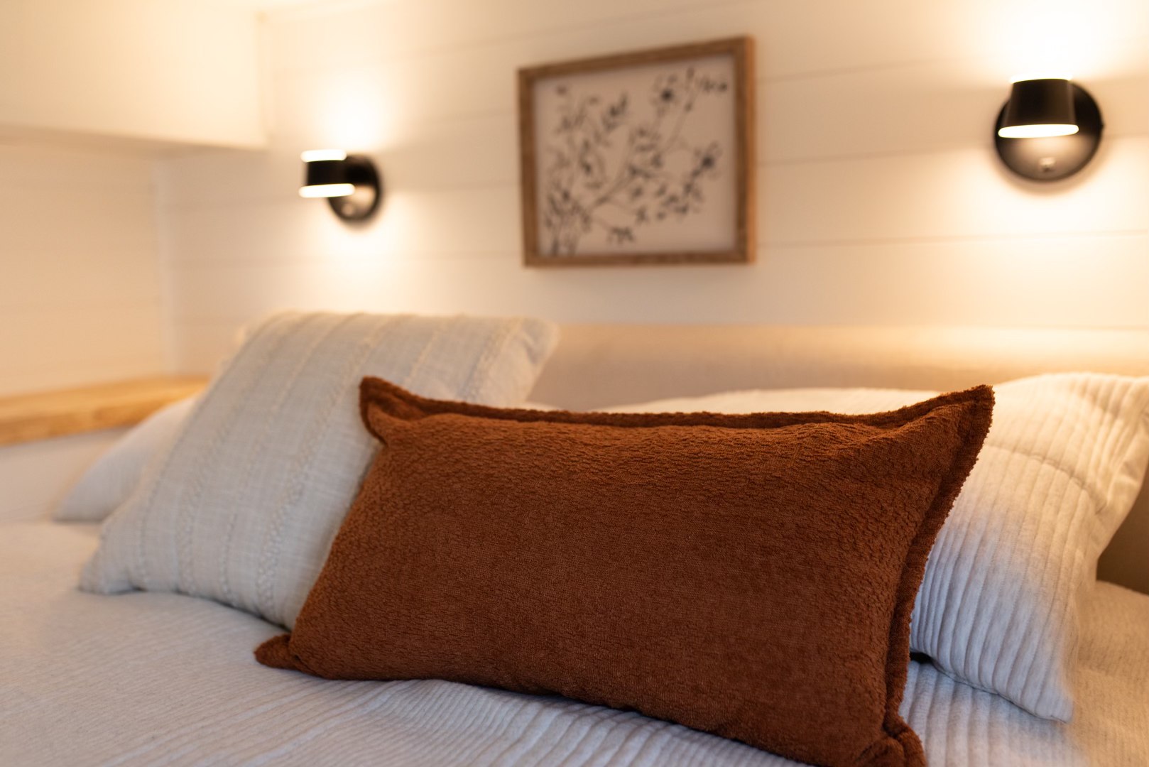 Cozy RV rental bedroom featuring a bed with white and rust-colored pillows, ambient wall lighting, and a framed botanical artwork.. Forest River Sunseeker LE 2006