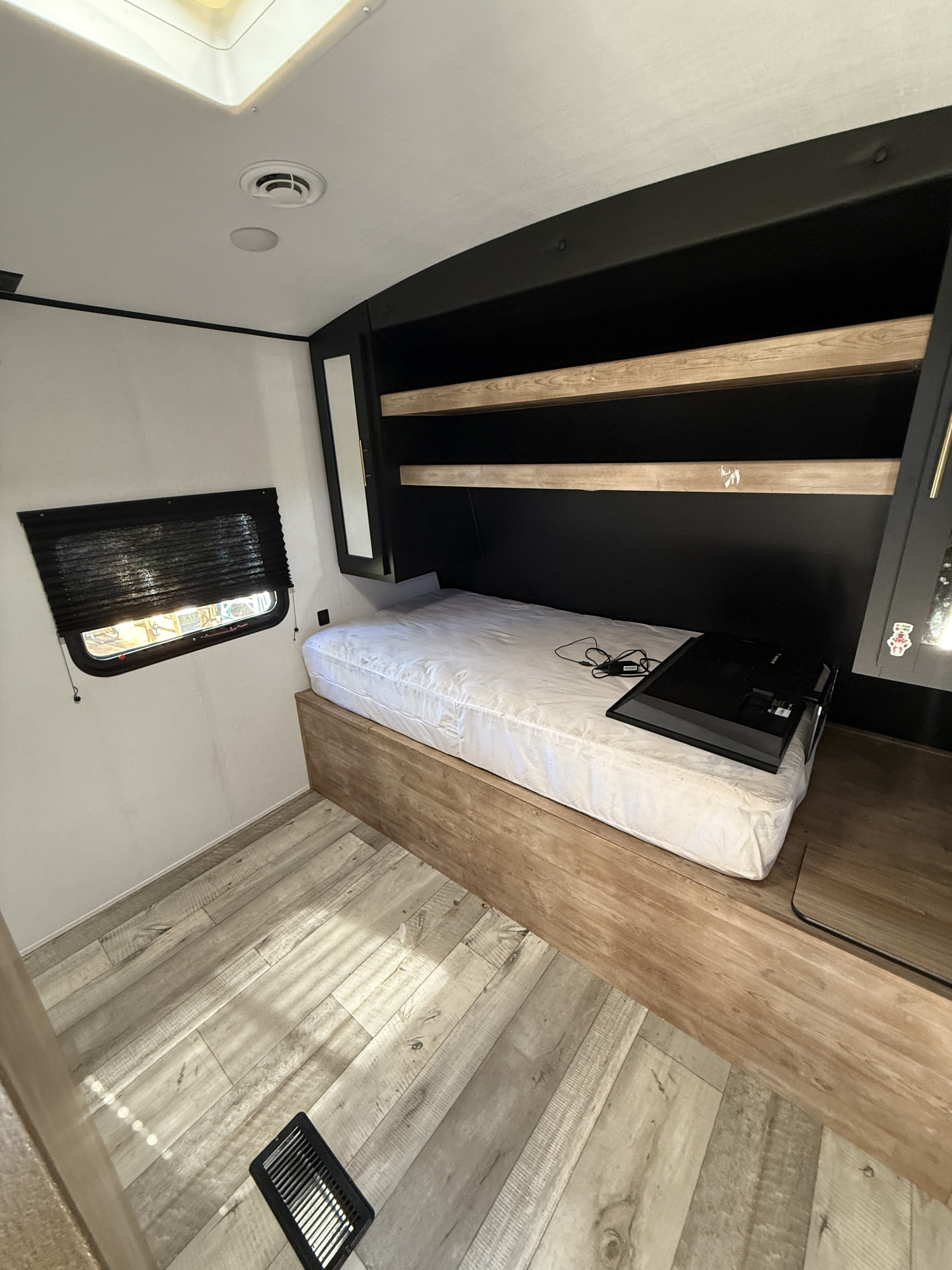 Cozy rv rental bedroom featuring a mattress on a wood base, sleek black shelving, and light wood flooring.. Keystone RV Springdale 2023