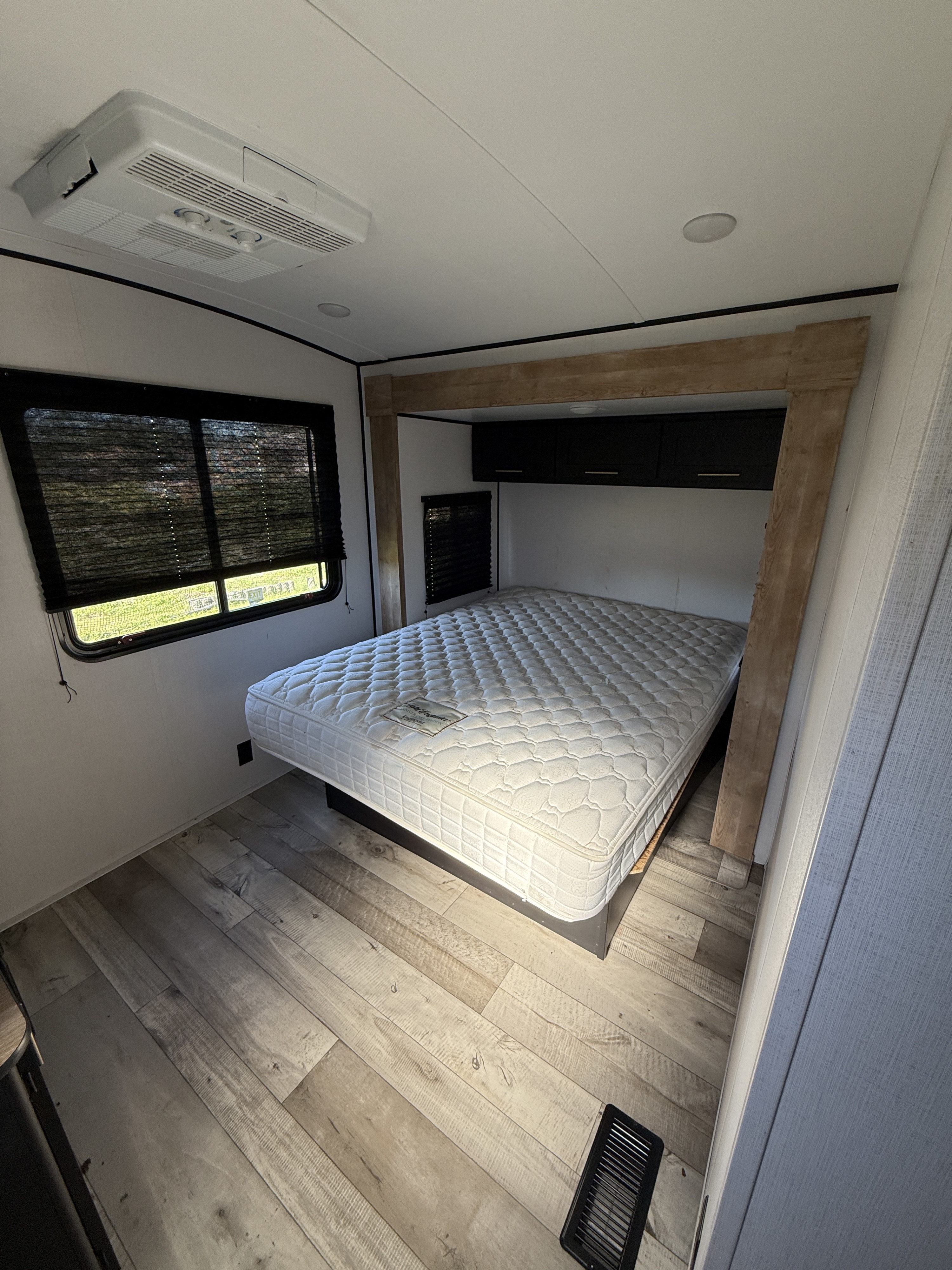RV rental bedroom: a cozy space featuring a bed, window, overhead AC, and wood-look flooring.. Keystone RV Springdale 2023