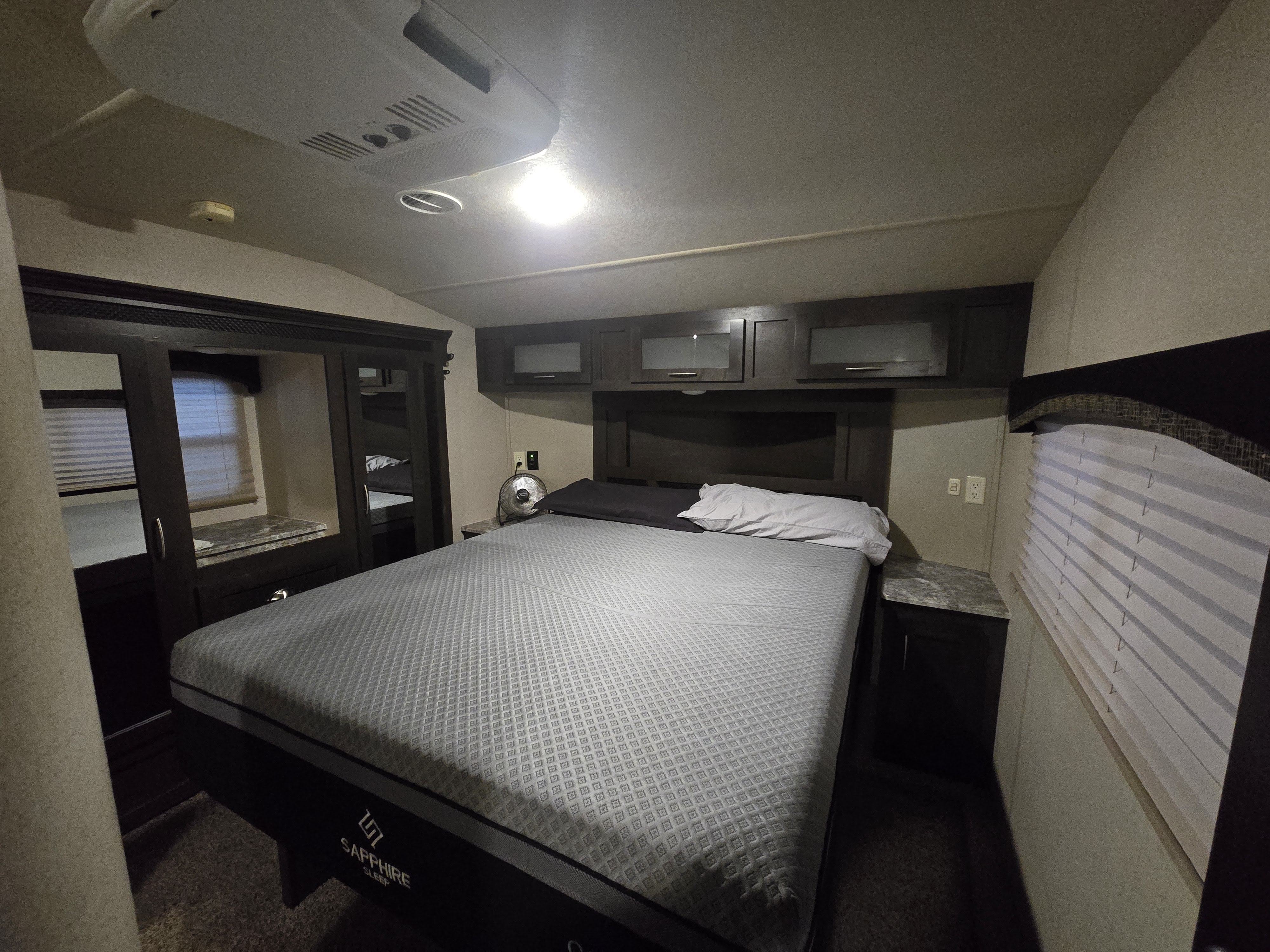Inside an RV rental: a cozy bedroom features a Sapphire Sleep mattress, cabinets, fan, and window blinds.. Forest River Shockwave 2018