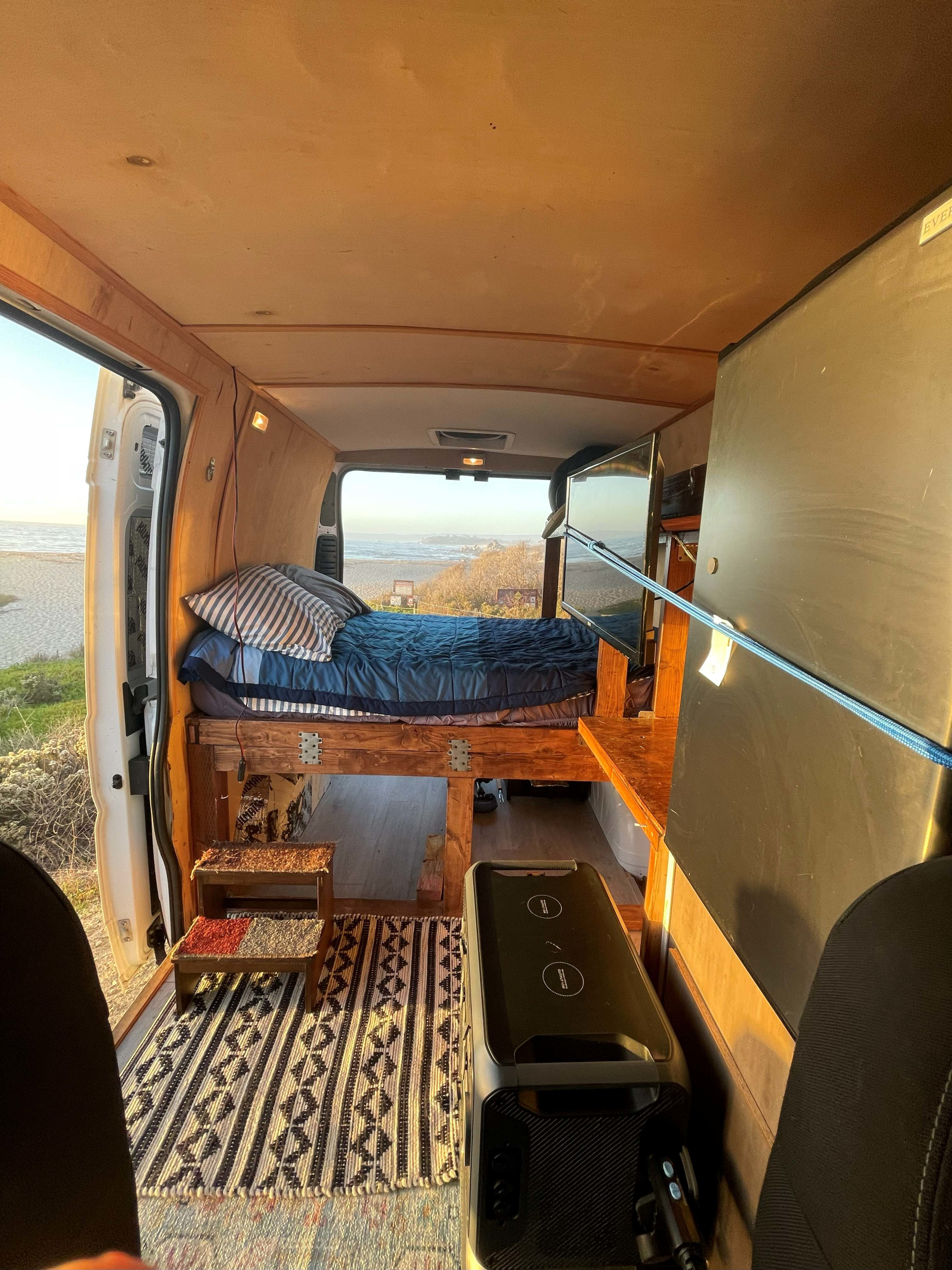 Cozy camper van interior with a bed, TV, and ocean view, ideal for an rv rental getaway.. Dodge 1500 2019