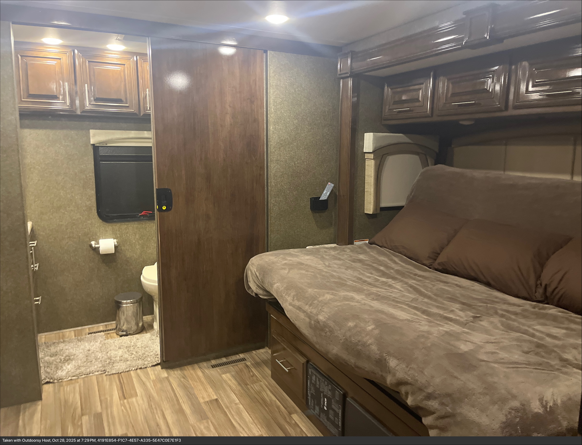 Cozy RV rental bedroom featuring a bed, overhead storage, and a private bathroom with a sliding door.. Thor Miramar 2019