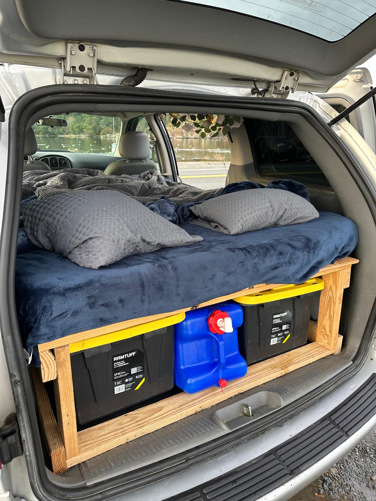 Minivan's cozy bed setup with under-bed storage & water jug, perfect for an RV rental and car camping.. Dodge Caravan 2005