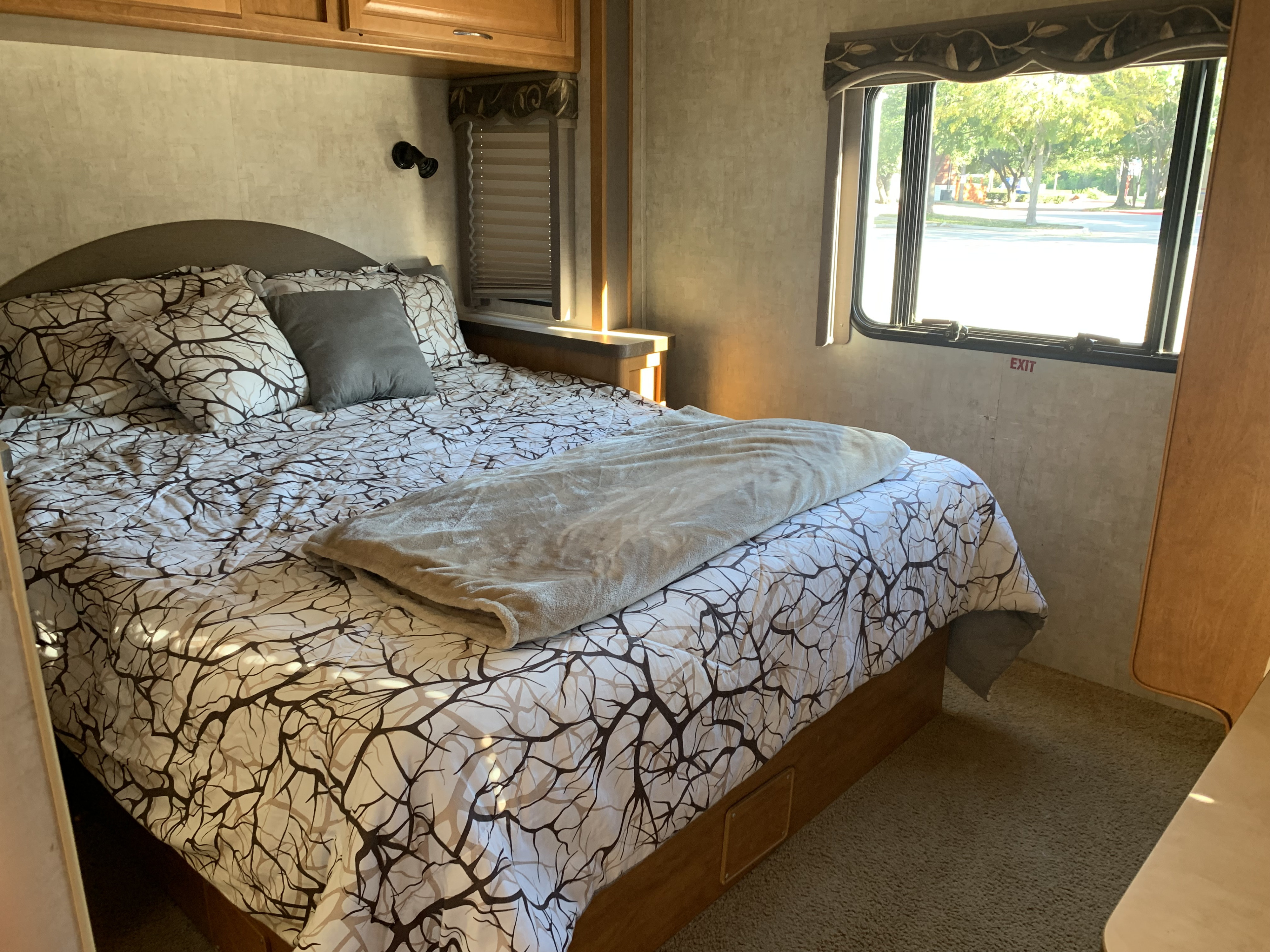This cozy rv rental bedroom features a comfortable bed with distinctive branch-patterned bedding and a window view of trees.. Jamboree Jamboree Motorhome 2006