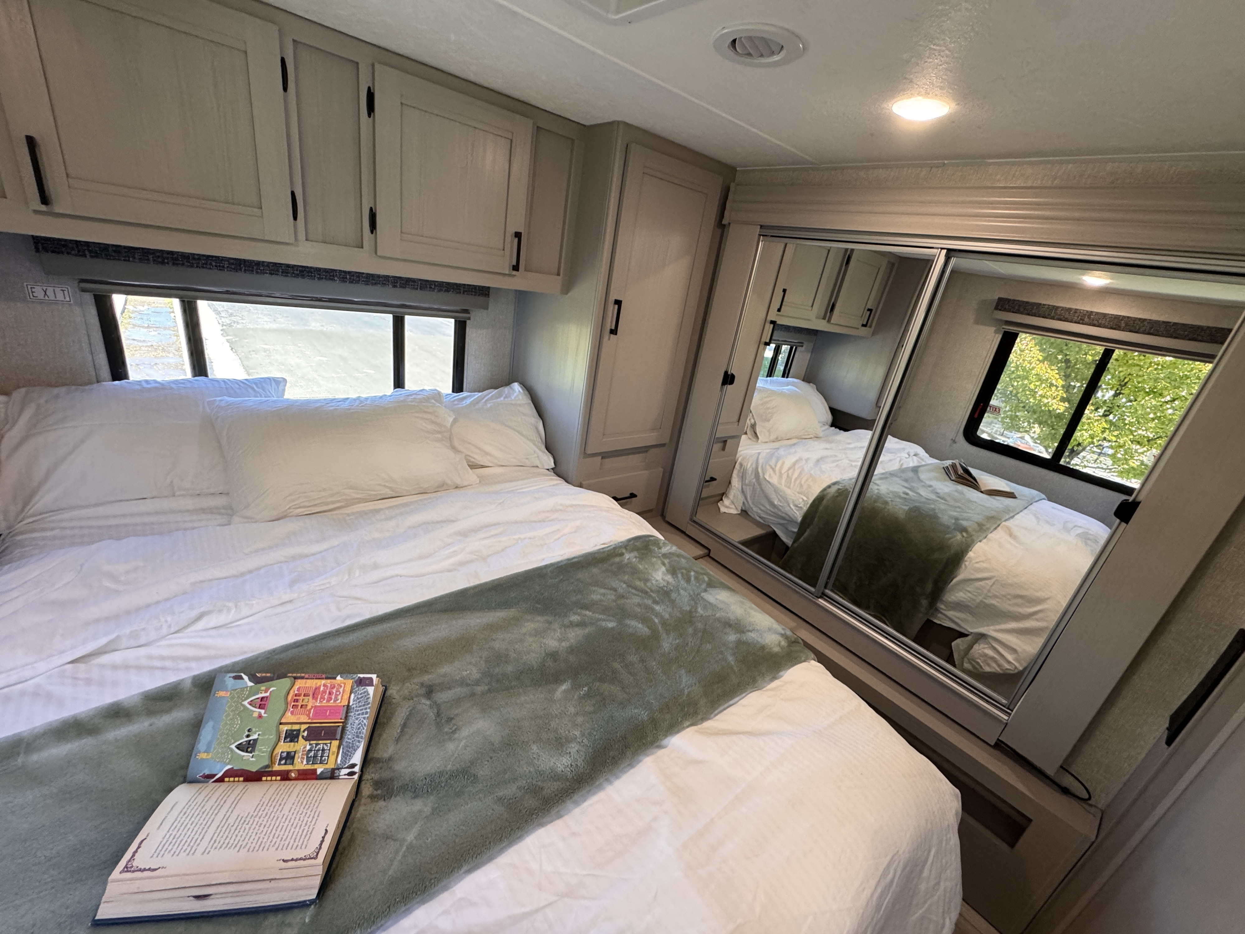 This RV rental features a comfortable bedroom with a white-linen bed, a green throw, and a large mirrored wardrobe.. Forest River Coachmen Freelander 2025