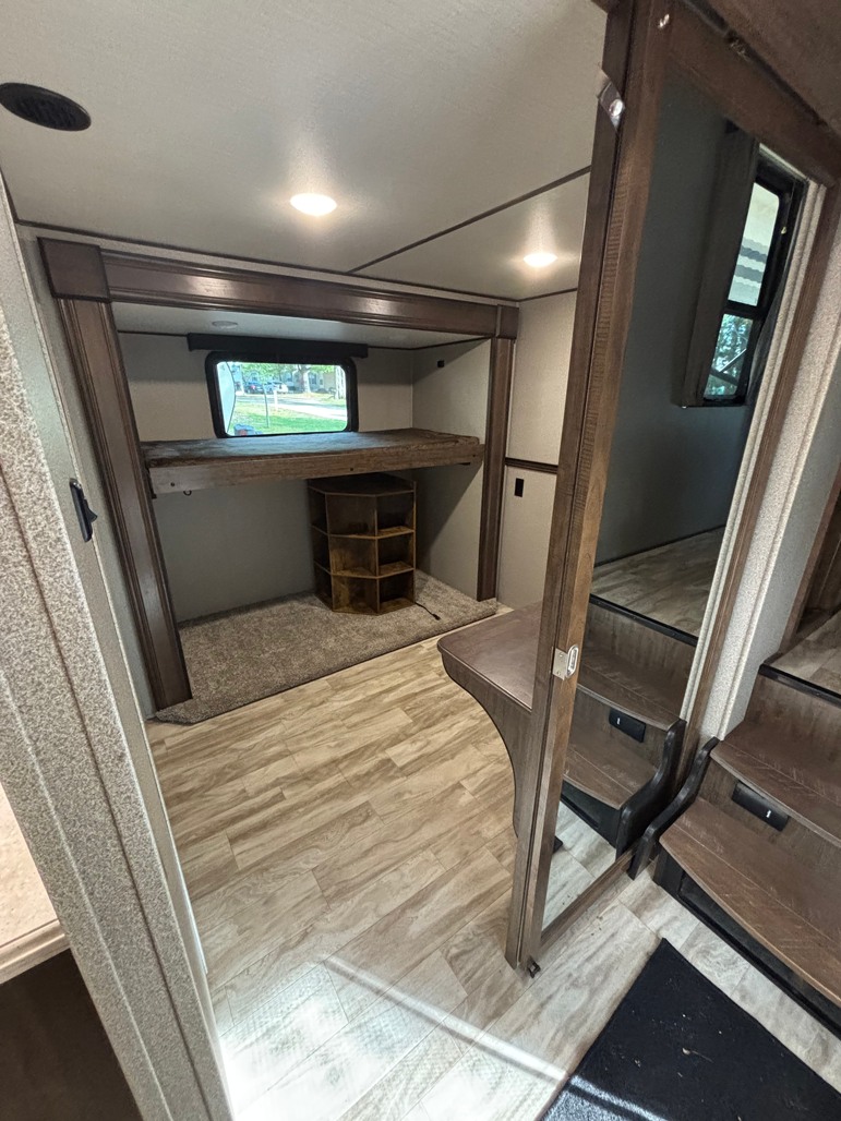 This RV rental features a bunk bed compartment with a window and small shelf, plus wooden steps leading to another section.. Grand Design Solitude 2021