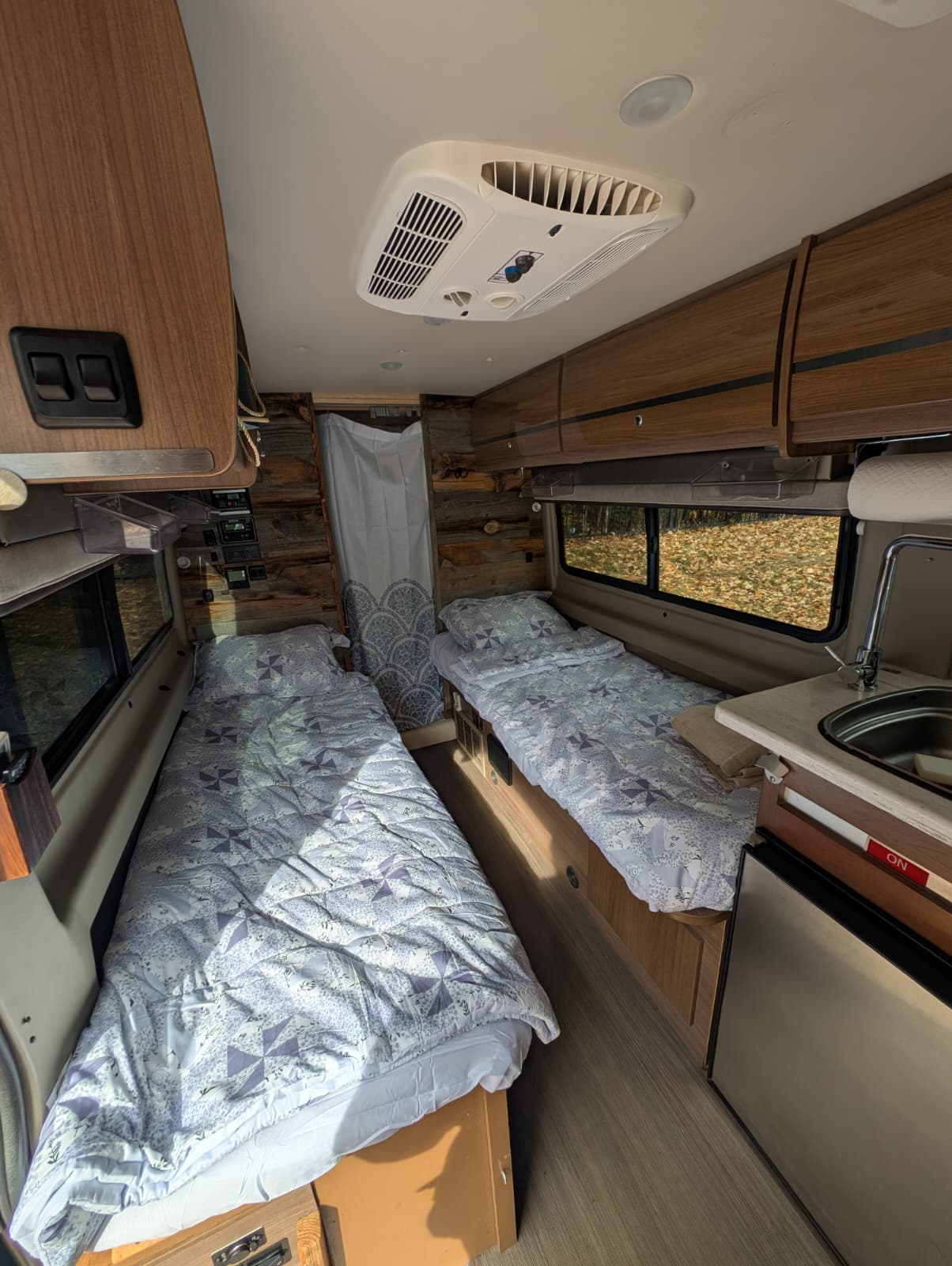 Inside an rv rental: twin beds, kitchenette, AC, and wood paneling create a cozy living space for travelers.. Winnebago Travato 2016