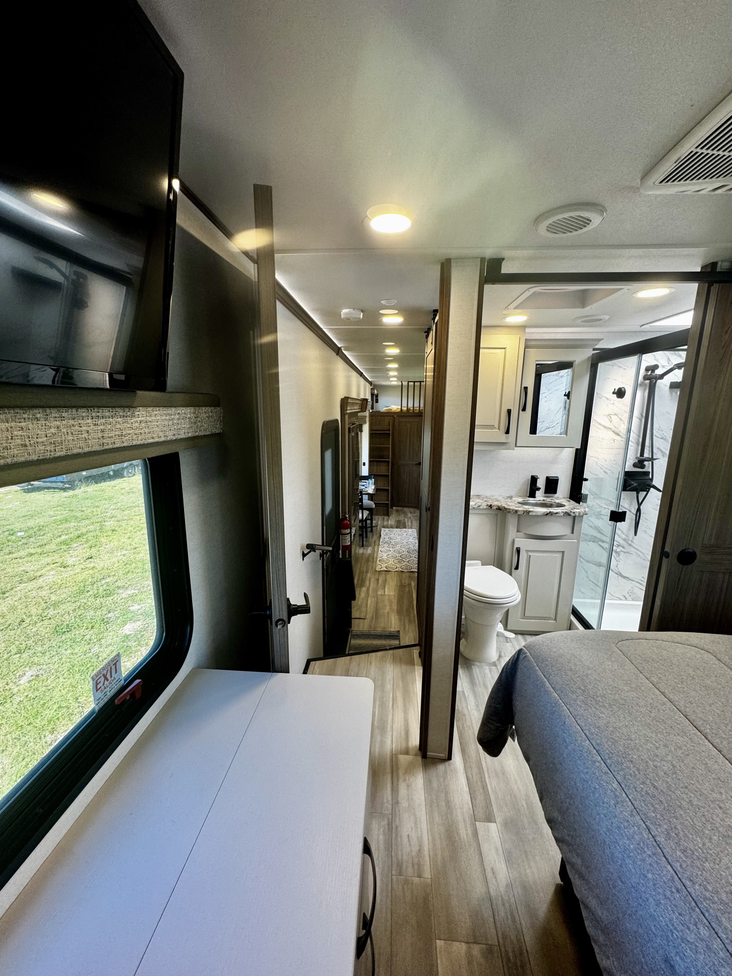 Modern RV rental interior with bedroom (right), bathroom (center), and hallway leading to the living area. TV on left.. Alliance RV Paradigm 2024