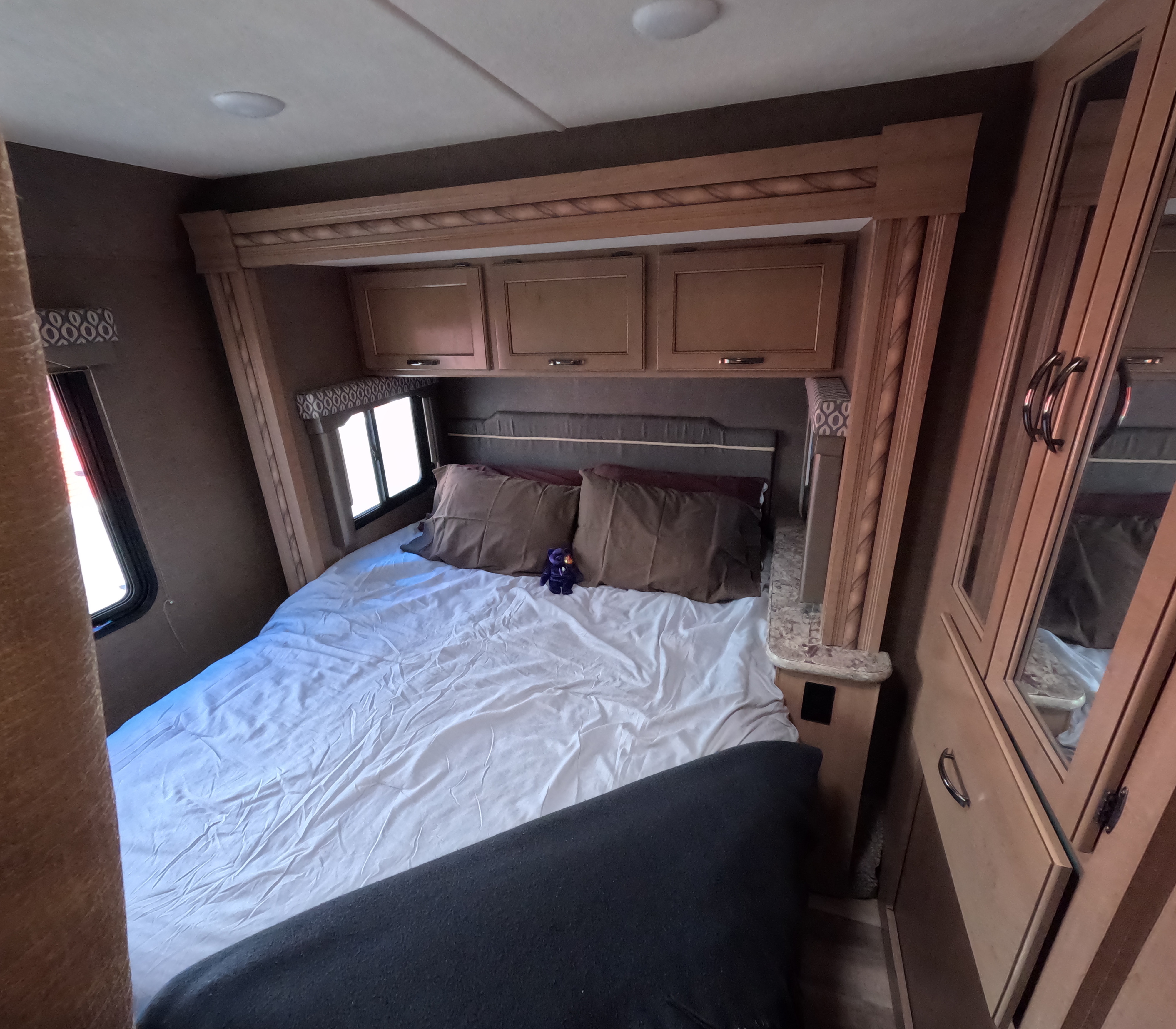 Cozy RV rental bedroom with queen bed, overhead storage, side window, and mirrored wardrobe.. Thor Freedom Elite 2018
