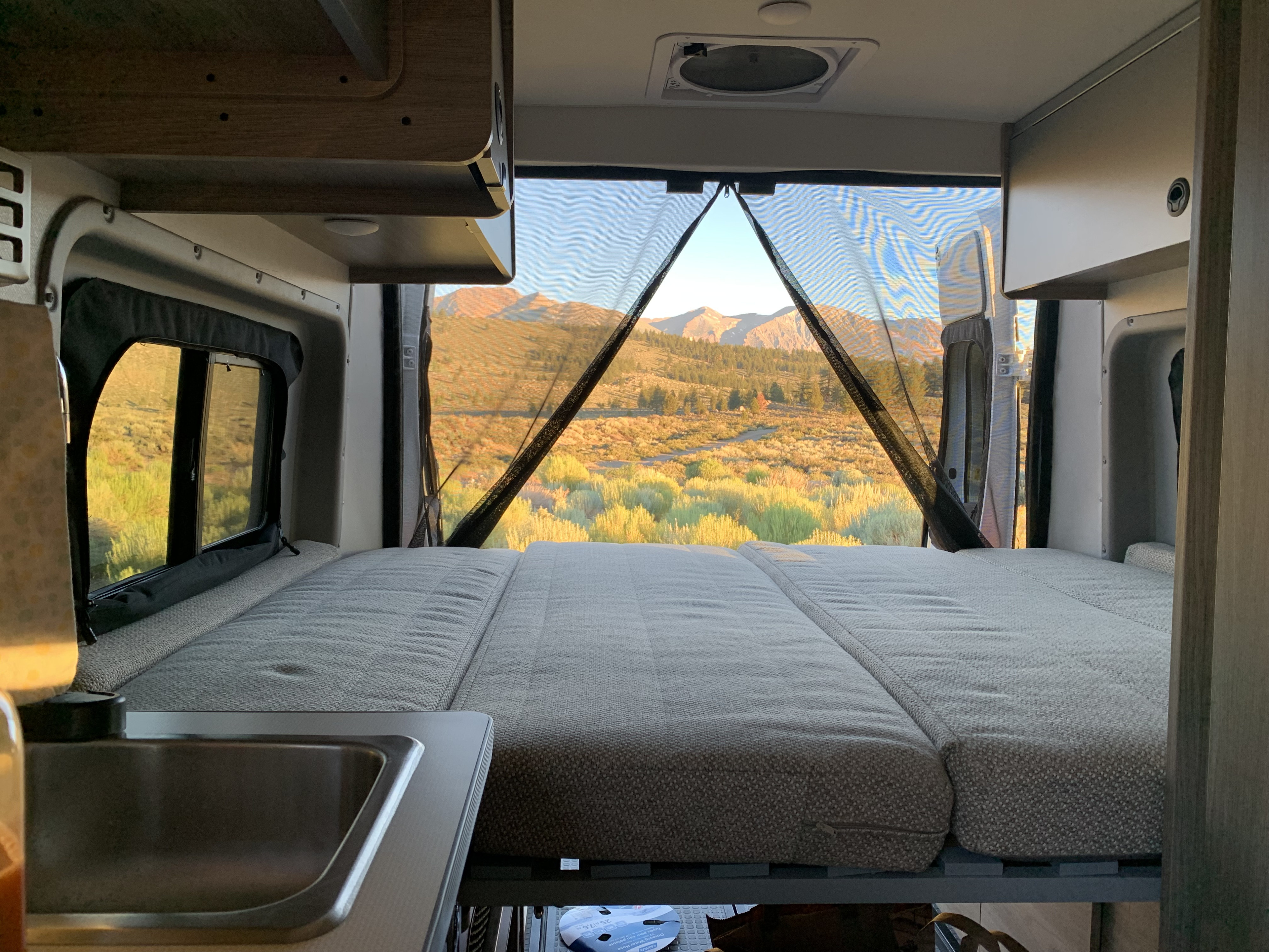 Cozy RV rental interior: bed, sink, and an incredible mountain view through the rear door screen. Ideal for nature travel.. Winnebago Solis 59P 2023