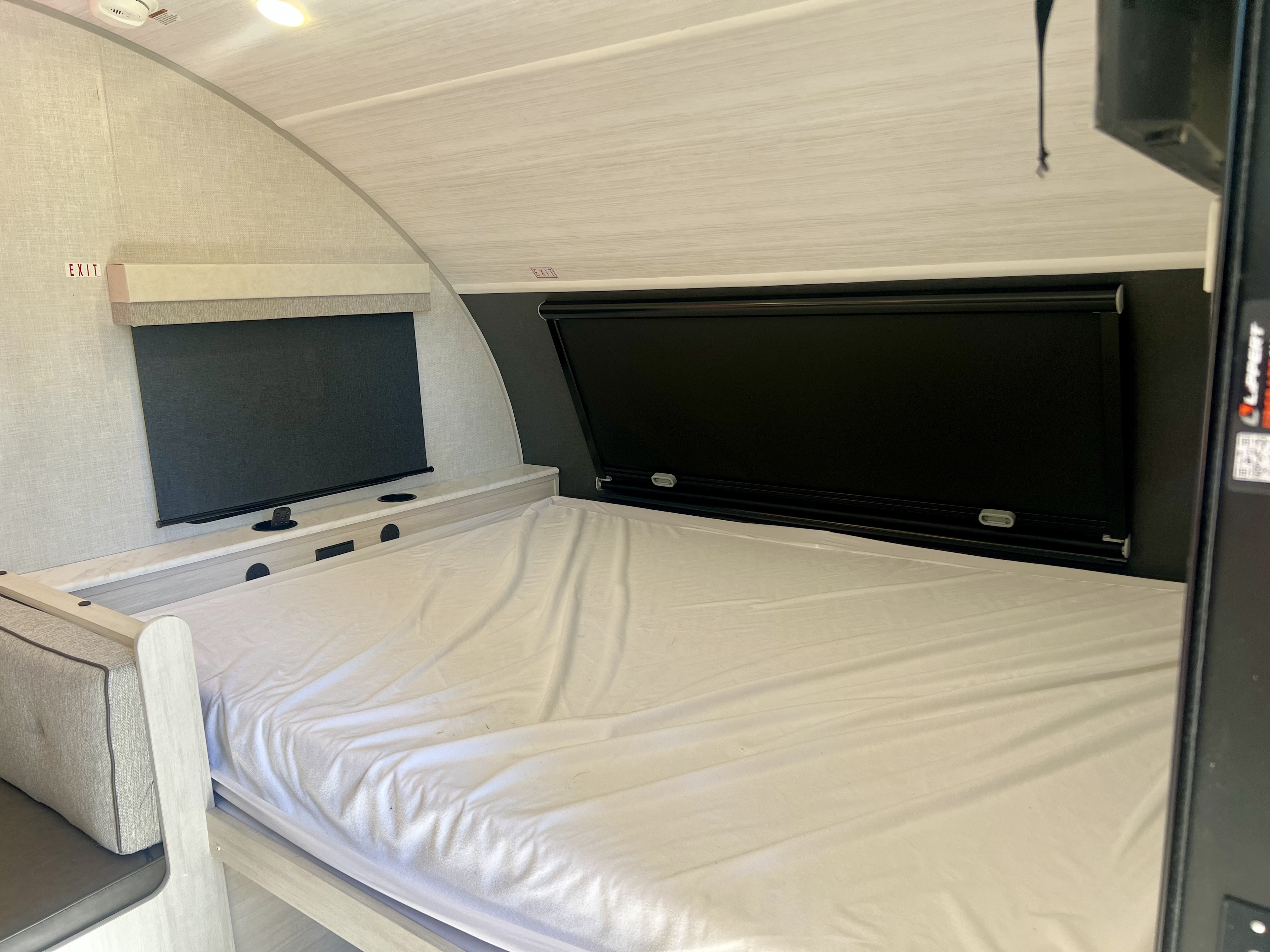 Interior of an RV rental bedroom featuring a bed with white sheets, black privacy blinds, and a built-in counter with cupholders.. Forest River R Pod 2026