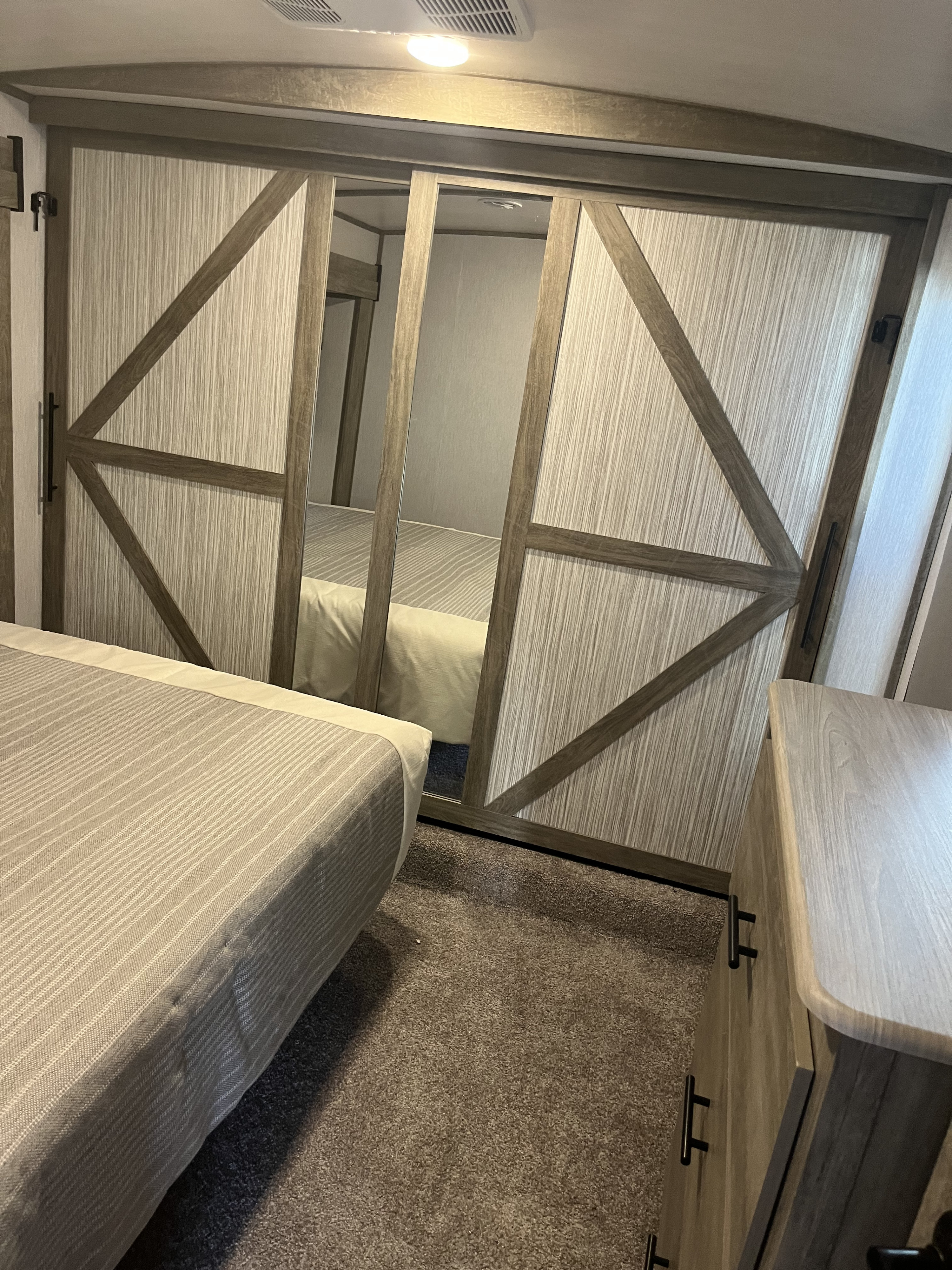 This RV rental bedroom features a comfy bed, a mirrored sliding closet with barn-style doors, and a dresser on carpet.. Forest River Wildwood Heritage Glen 2022