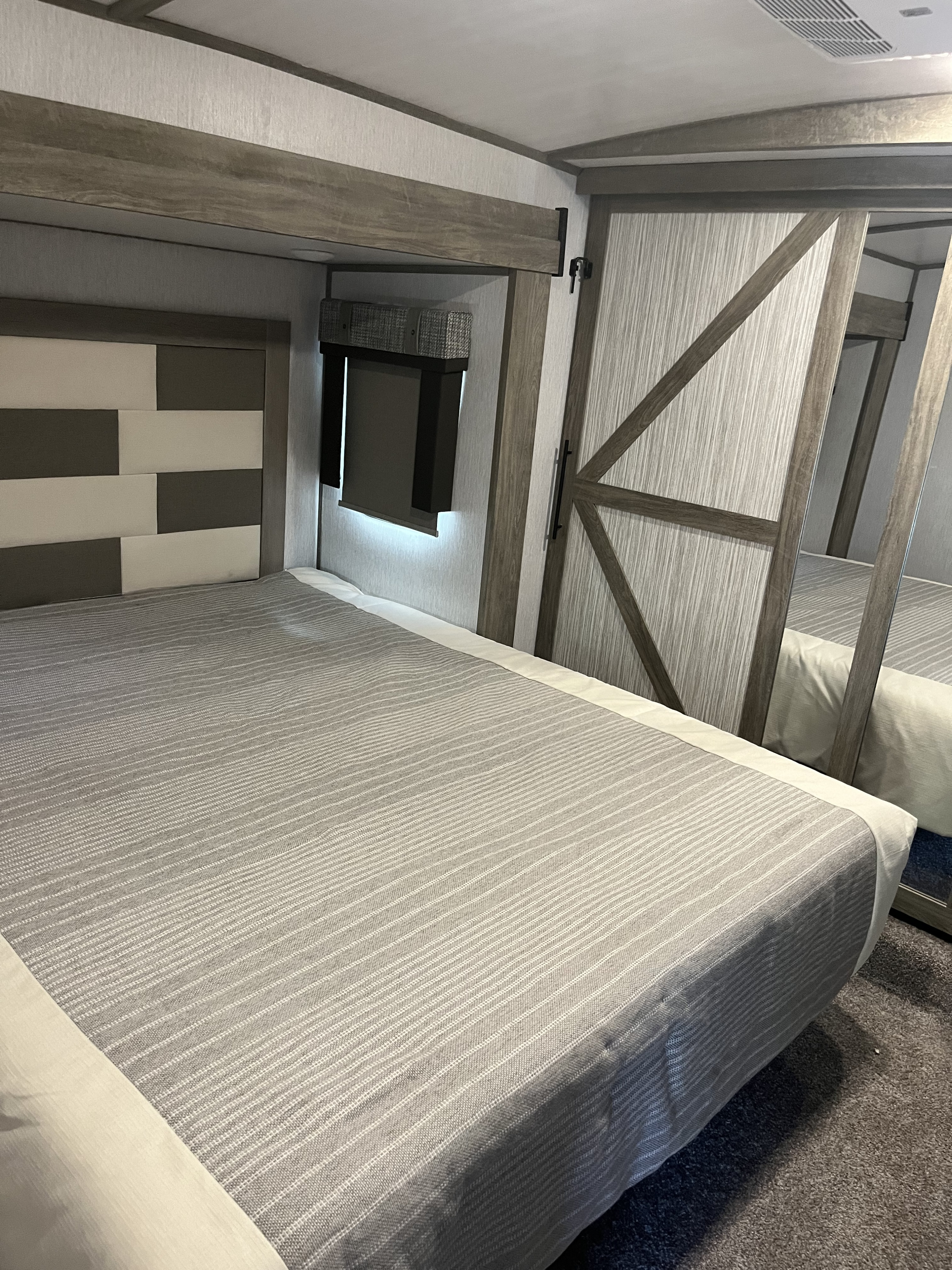 This spacious RV rental bedroom features a comfy bed with striped bedding, a modern headboard, and a mirrored barn door.. Forest River Wildwood Heritage Glen 2022