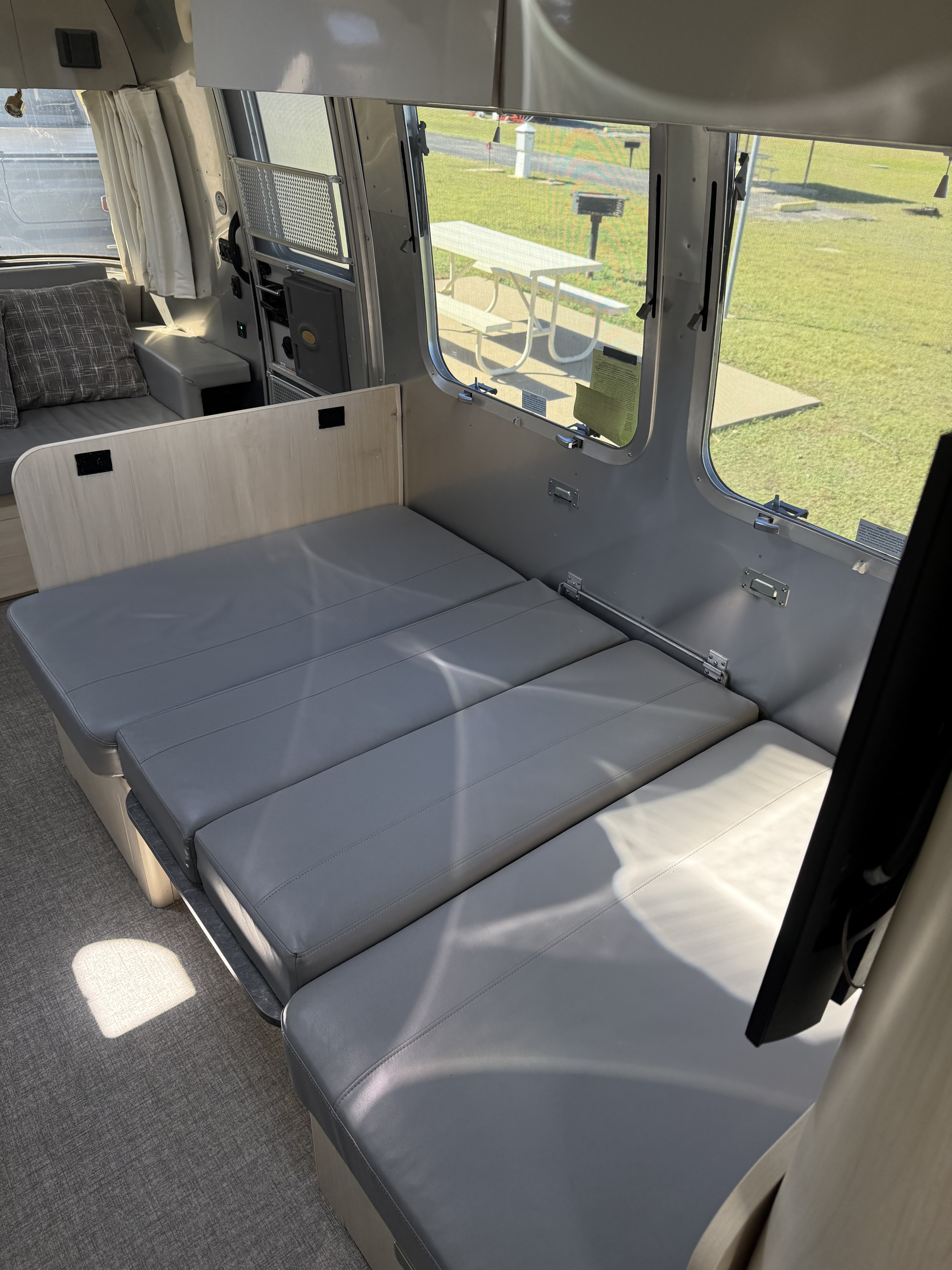 Enjoy the versatile interior of this RV rental, featuring a convertible bed/dinette with gray cushions and bright park views.. Airstream Flying Cloud 2022