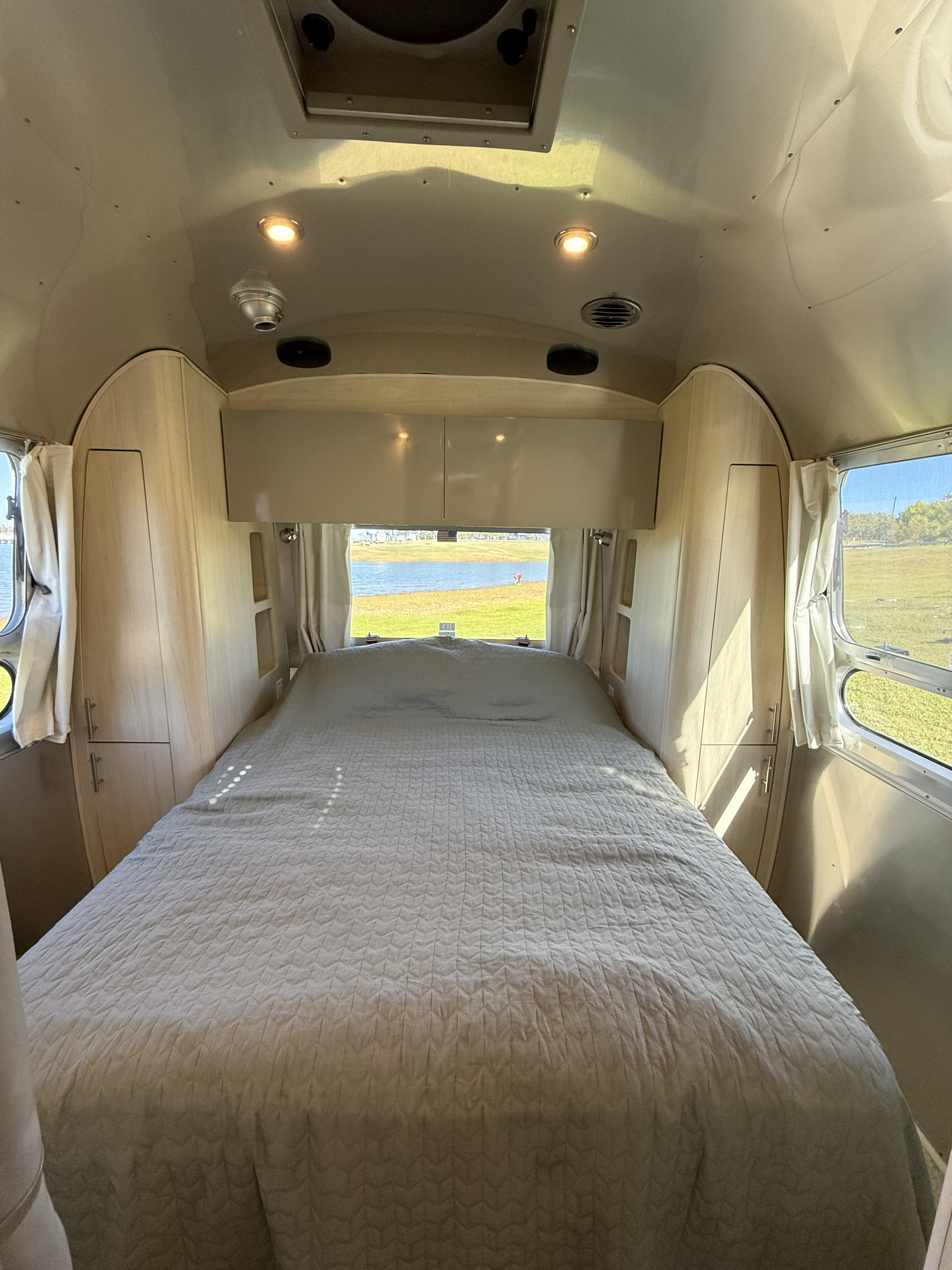 Cozy Airstream RV rental bedroom with a lake view, featuring a plush bed and light wood interior. Ideal for your next adventure!. Airstream Flying Cloud 2022