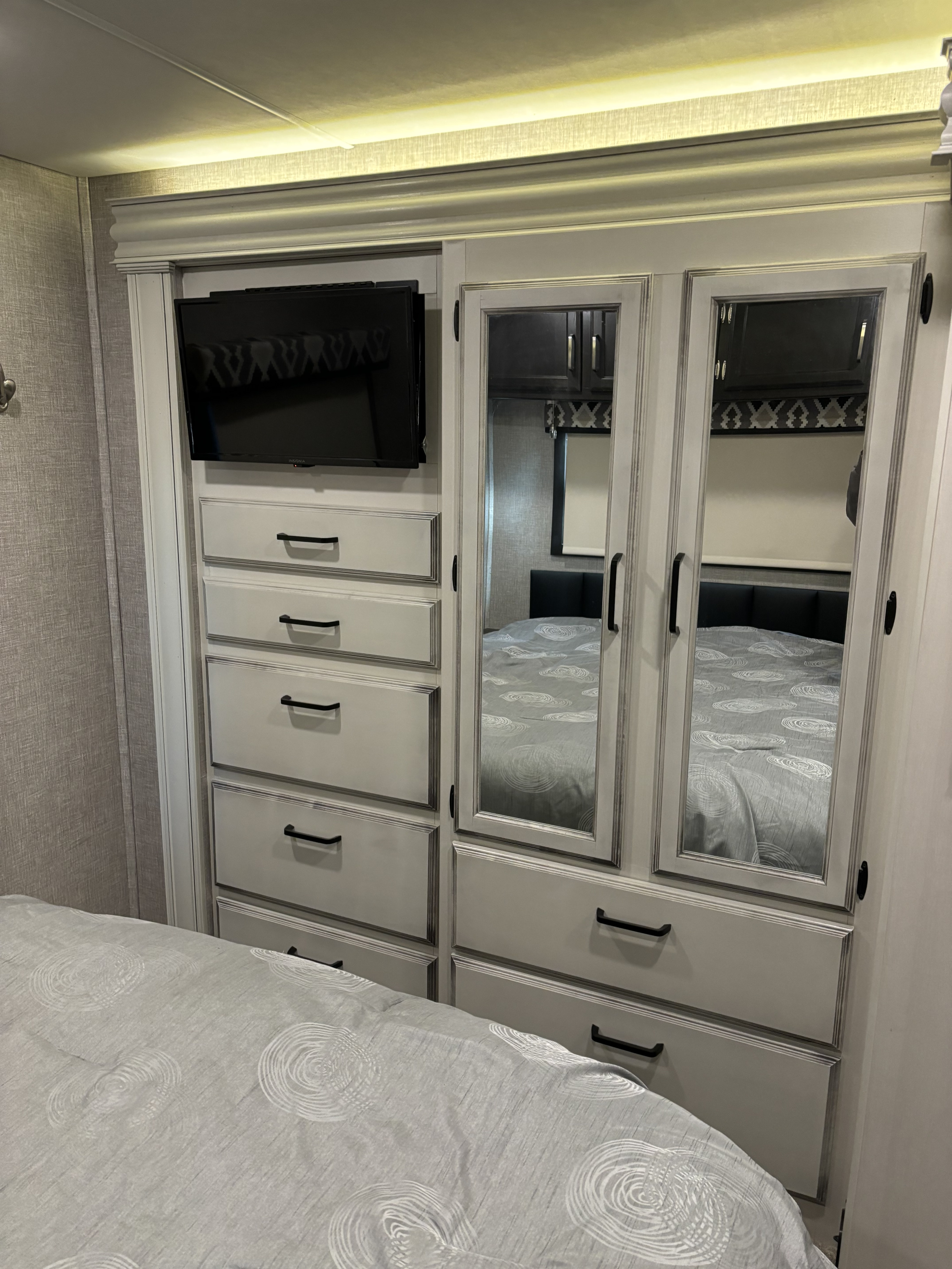 RV rental bedroom with TV, drawers, and mirrored wardrobe reflecting the bed and indirect lighting.. Jayco Greyhawk 2022