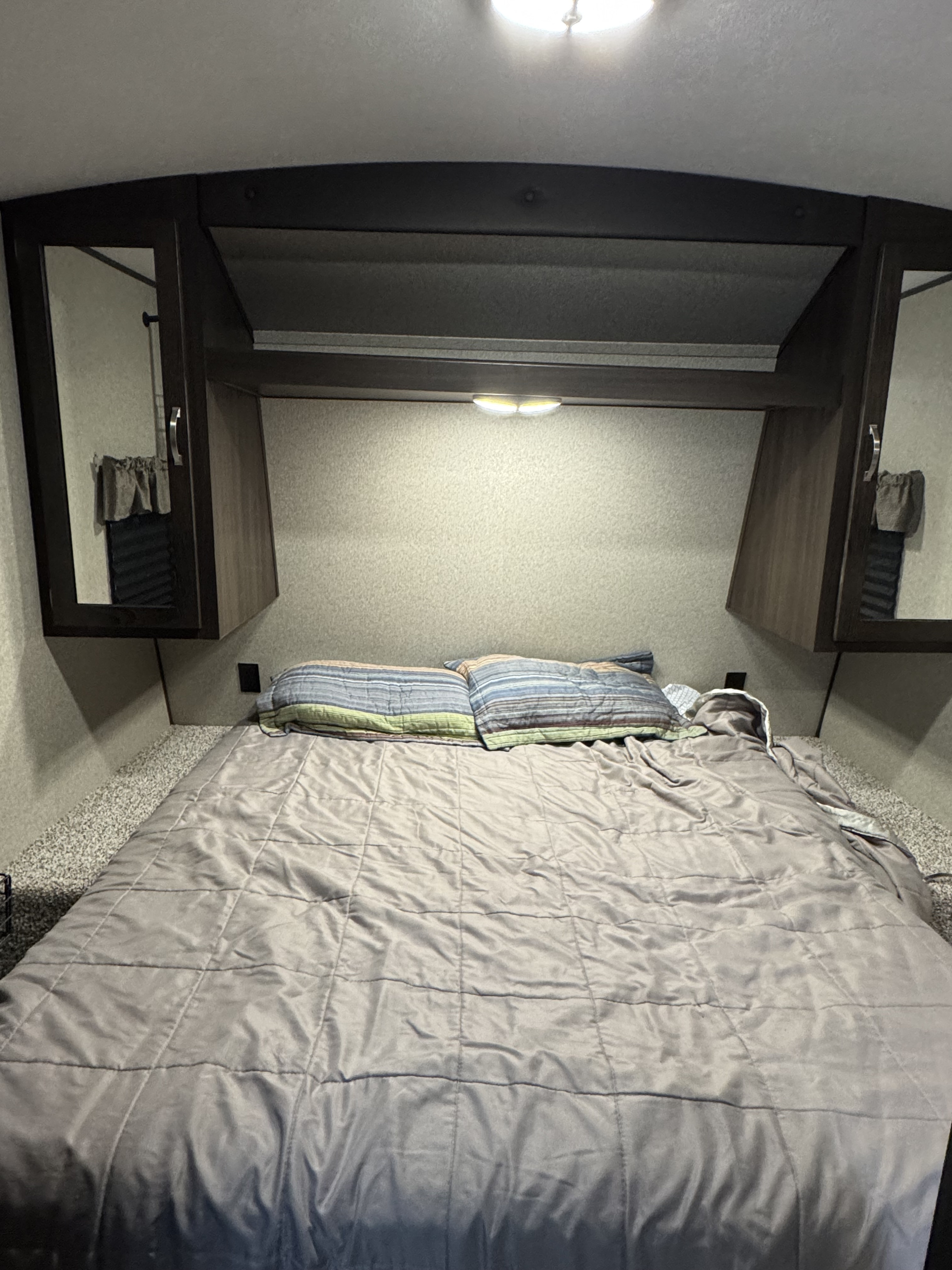 RV rental bedroom featuring a comfortable bed with striped pillows, overhead cabinets, and functional lighting.. Keystone RV Springdale 2020