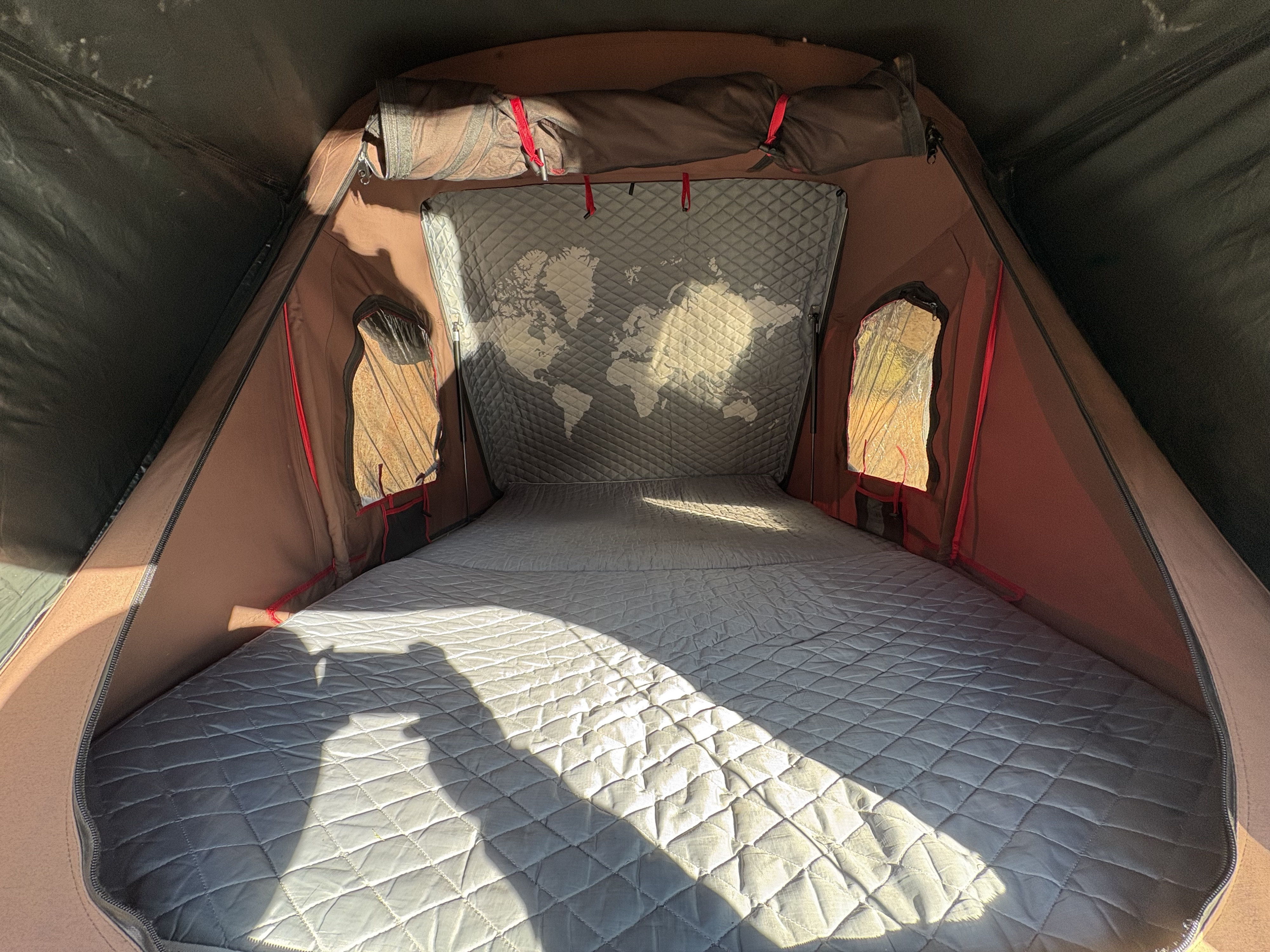 Cozy rv rental rooftop tent interior with a quilted mattress, world map wall, and side windows, perfect for camping trips.. Toyota 4 Runner SR5 2010