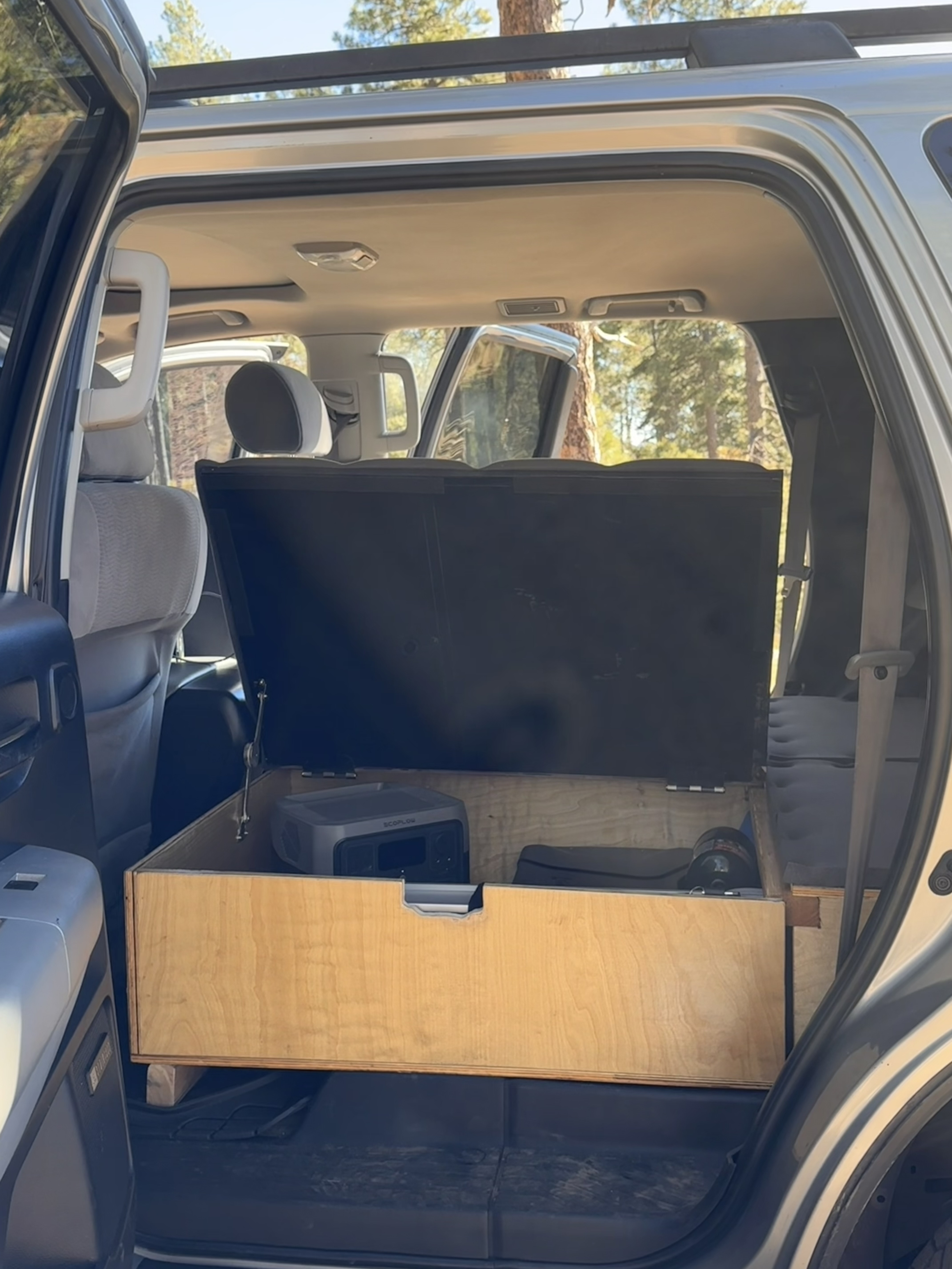 Inside an RV rental: a custom car camping setup with a wooden storage box, EcoFlow portable power, & folded seats.. Toyota Dreamseeker Voyager 2008