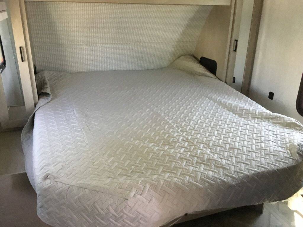 Comfortable bed in an RV rental, with a light quilted bedspread and integrated headboard, ready for your trip.. Forest River Wildwood X-Lite 2024