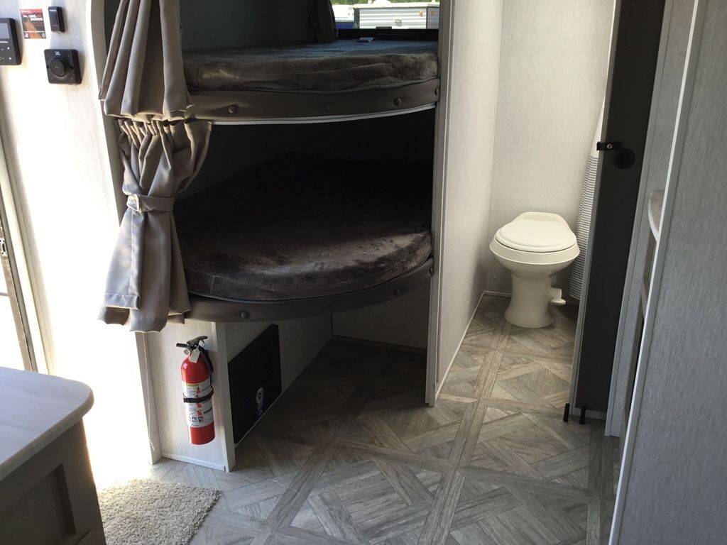 An rv rental interior featuring bunk beds with privacy curtains, a toilet in a small bathroom, and a fire extinguisher for safety.. Forest River Wildwood X-Lite 2024