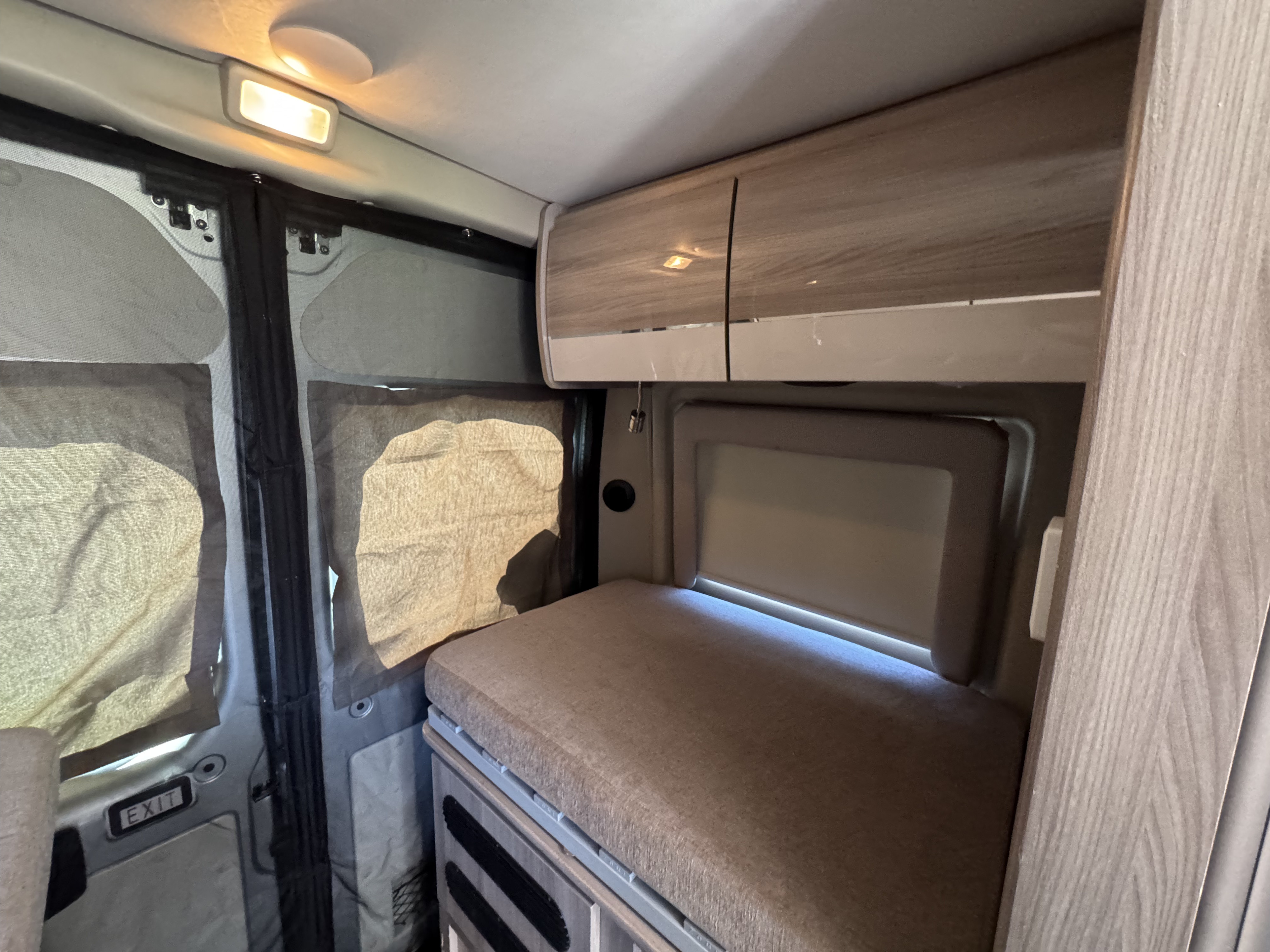 Modern rv rental interior featuring a cushioned bed, sleek overhead storage, and screened windows for comfortable journeys.. Dodge Ram 1500 2022