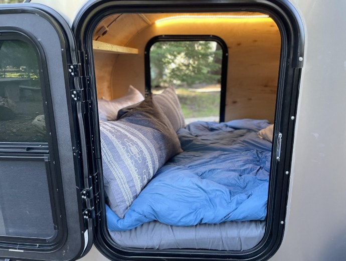Experience comfort in this RV rental teardrop camper. A cozy bed with blue bedding fills the compact, wood-paneled interior.. Bend Teardrop Teardrop 6x12 2023