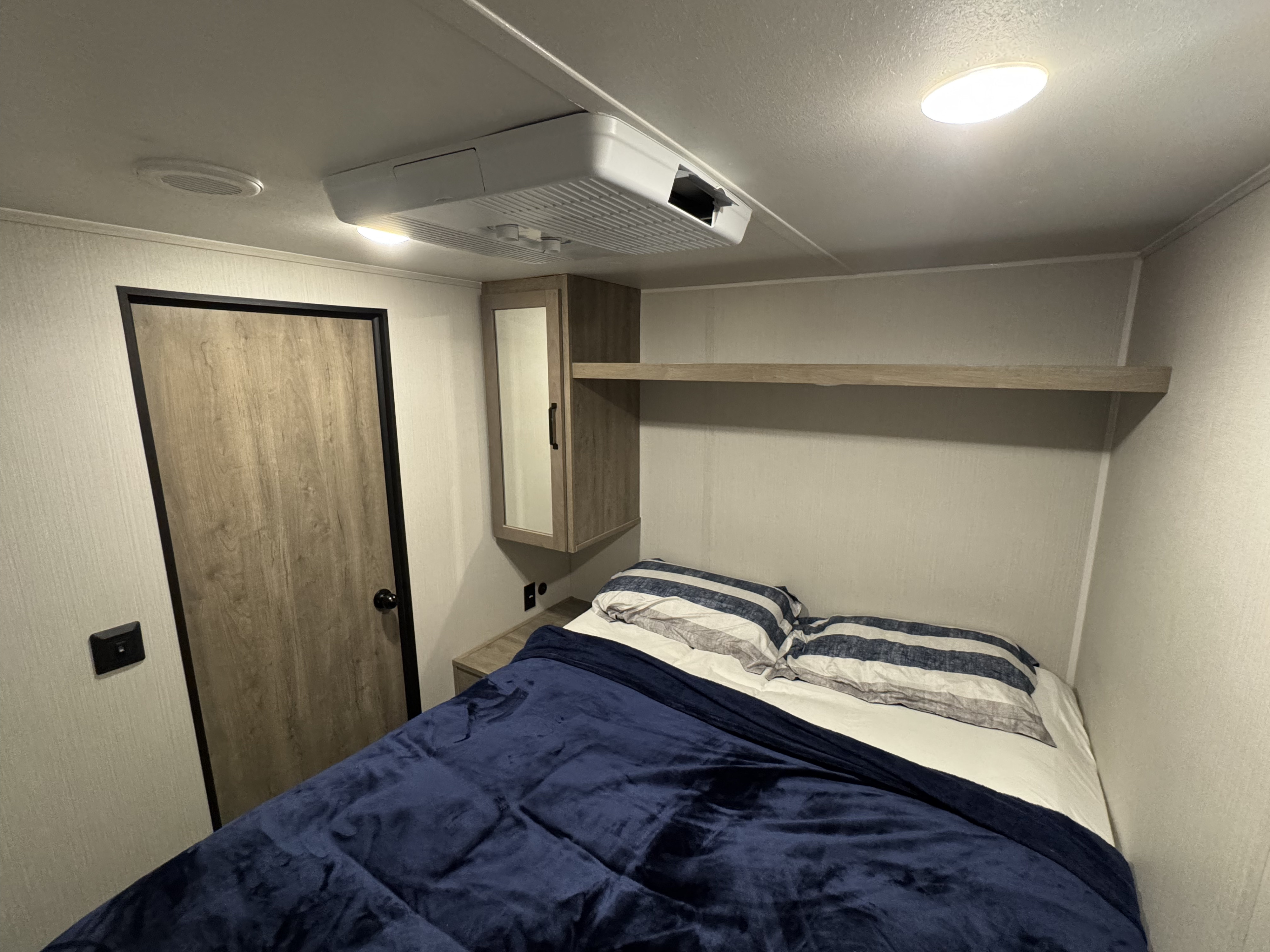 This RV rental bedroom features a cozy bed with striped pillows, overhead storage, an AC unit, and a mirrored cabinet.. Palamino Puma 2024