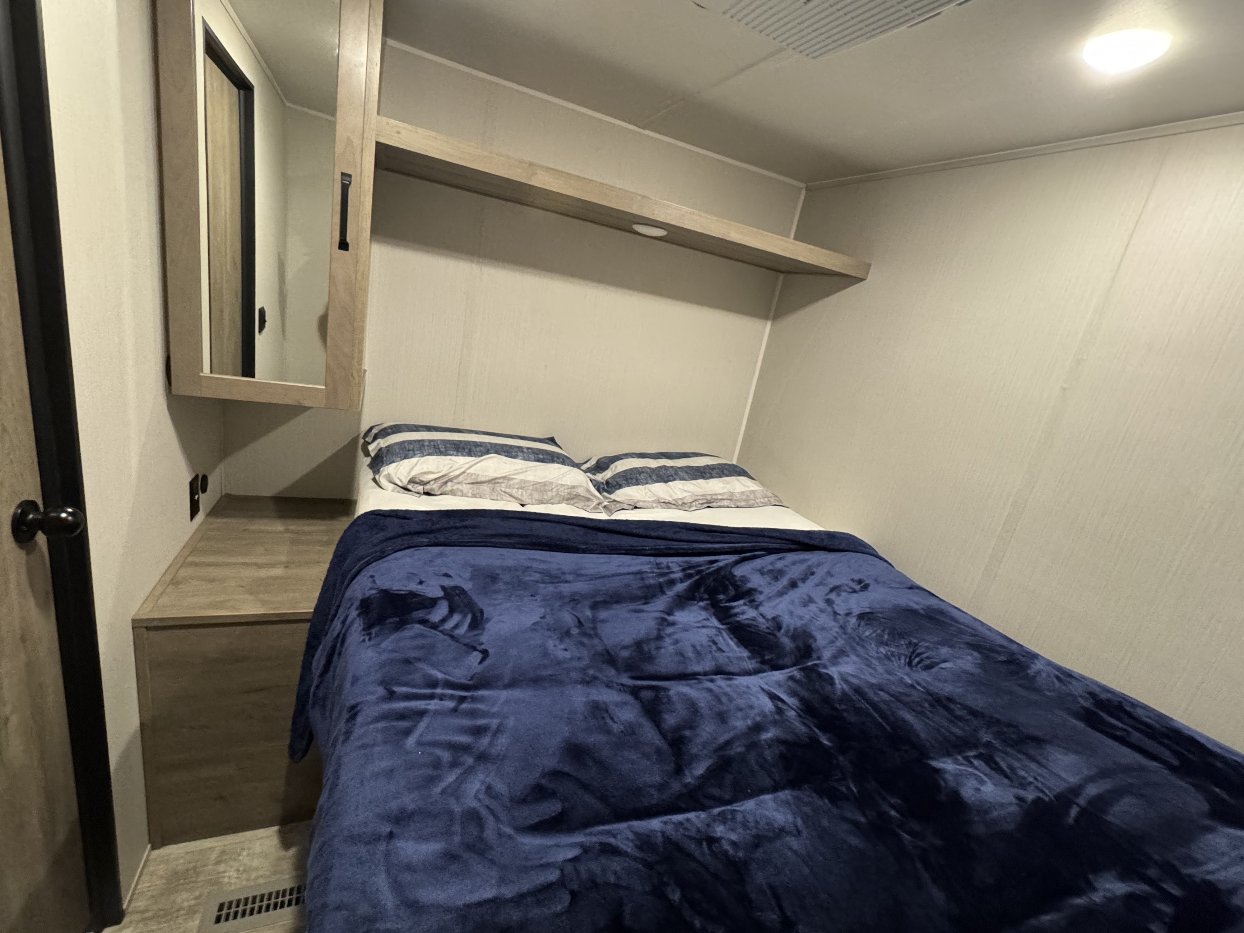 Cozy RV rental bedroom featuring a comfortable bed, overhead shelving, and a mirrored cabinet, ideal for compact travel.. Palamino Puma 2024