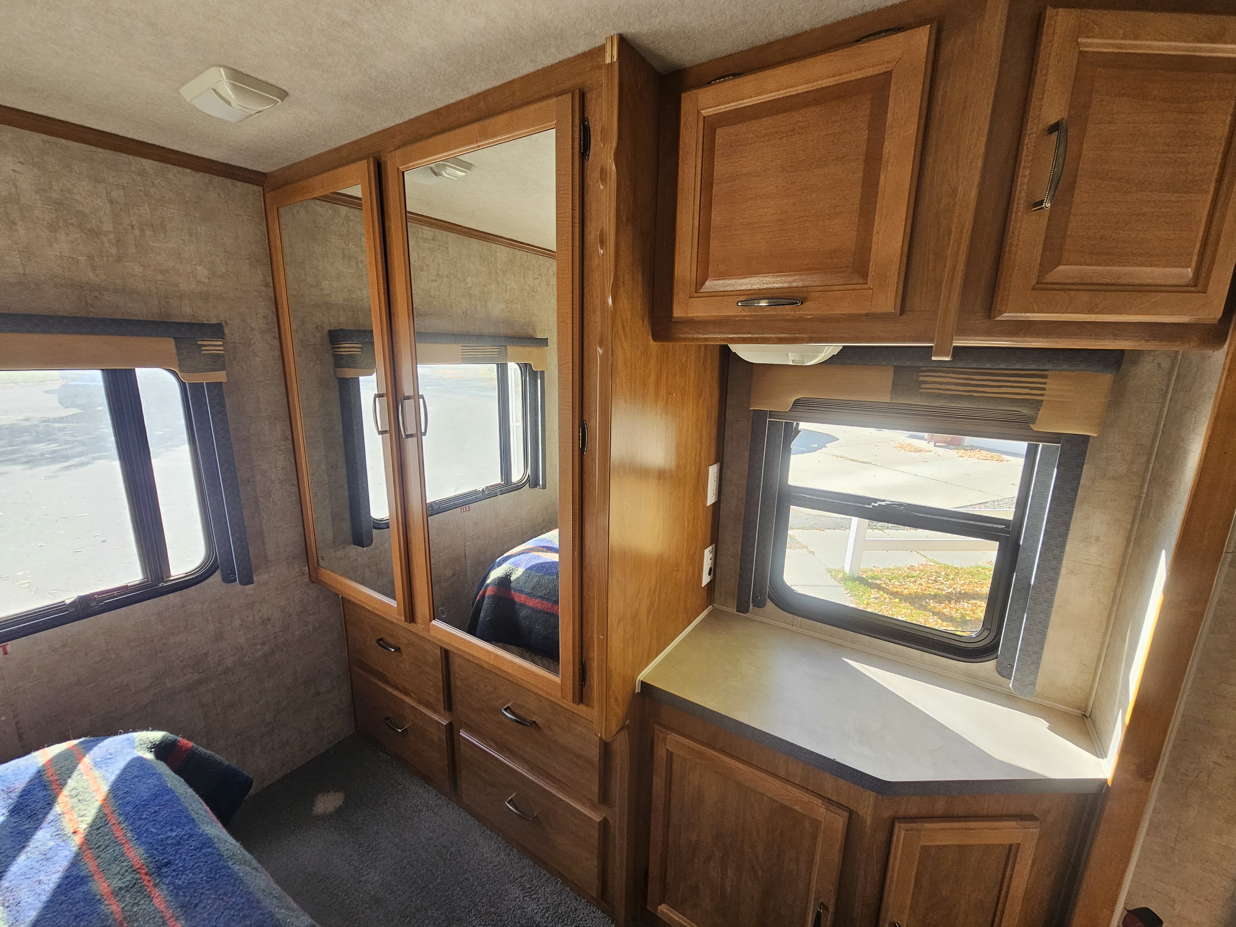 Cozy RV rental bedroom featuring wood cabinets, mirrored closet, drawers, windows with shades, and counter space.. Tioga SL 2006