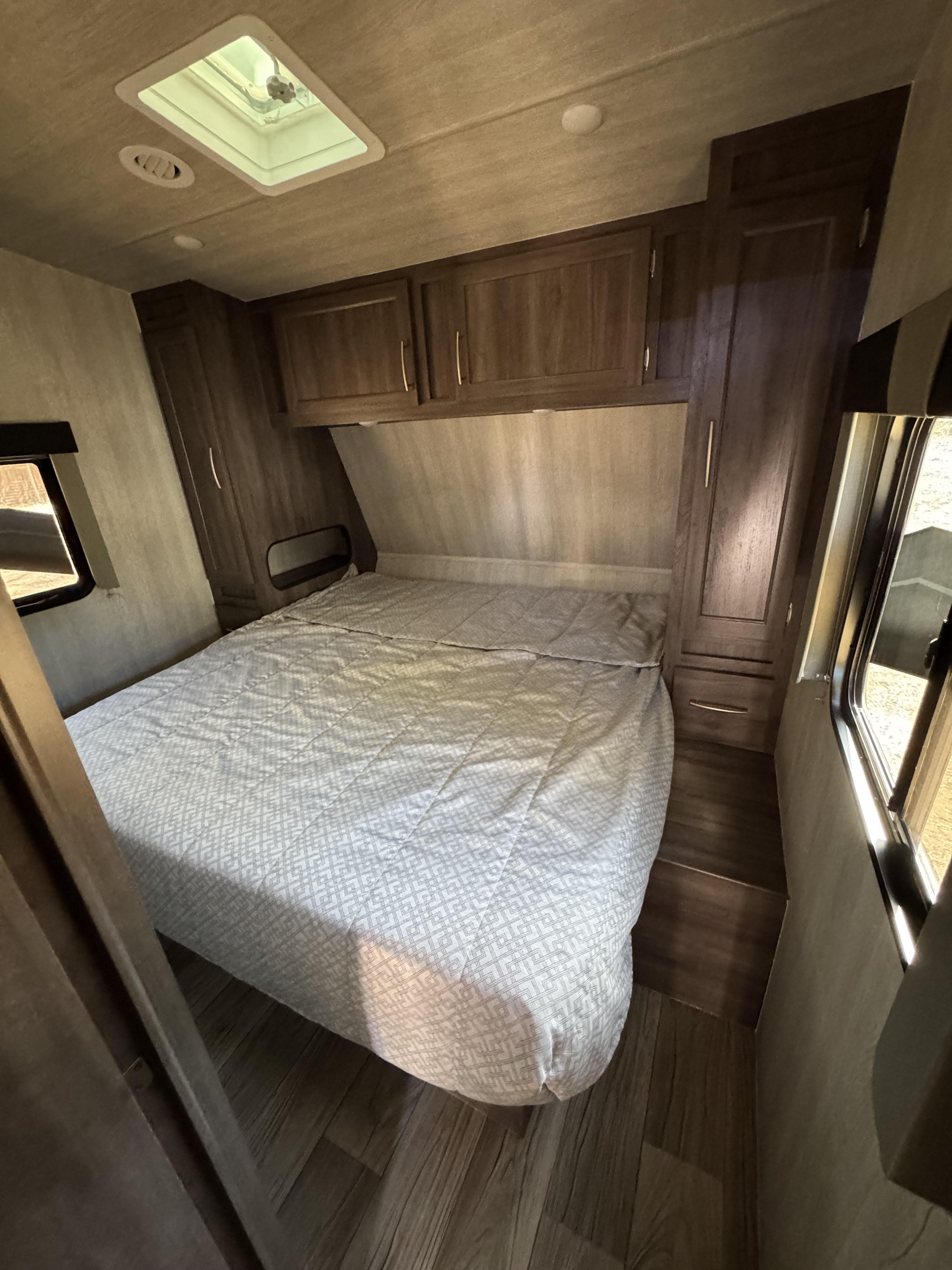 This RV rental bedroom features a comfortable bed, overhead cabinets, and side windows, ready for travel.. Genesis Supreme Rv Ragen 2025
