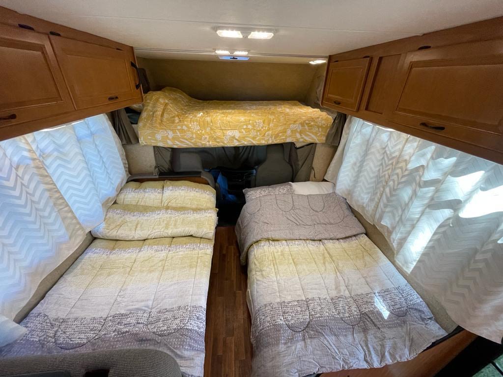 Cozy RV rental interior with a bunk bed, two single beds, overhead cabinets, and bright curtains, ideal for travel.. Other Other 2016