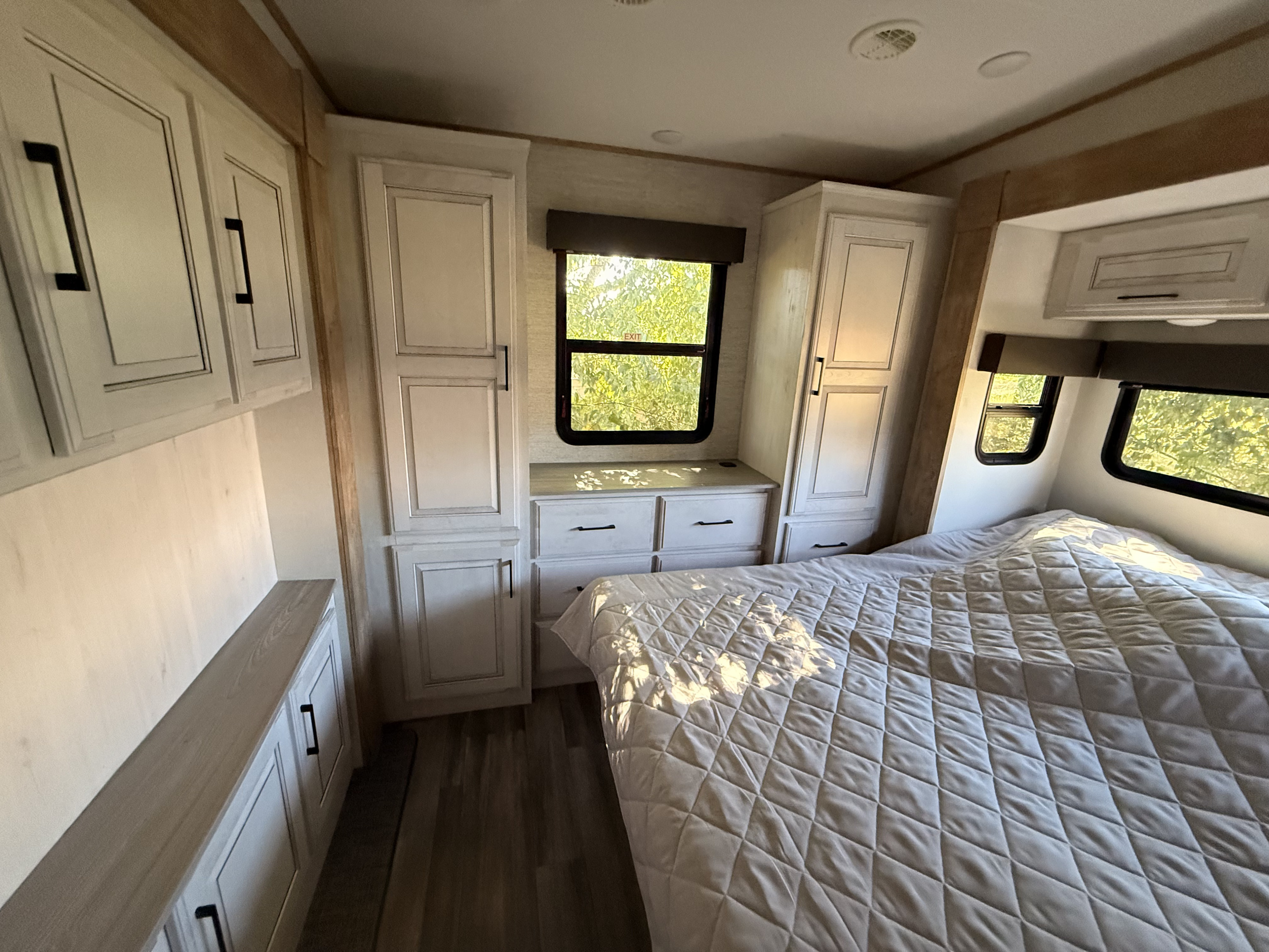 Clean rv rental bedroom interior, showcasing light wood-look cabinets, storage drawers, and a quilted bed by sunlit windows.. Heartland RVs Bighorn Traveler 2024