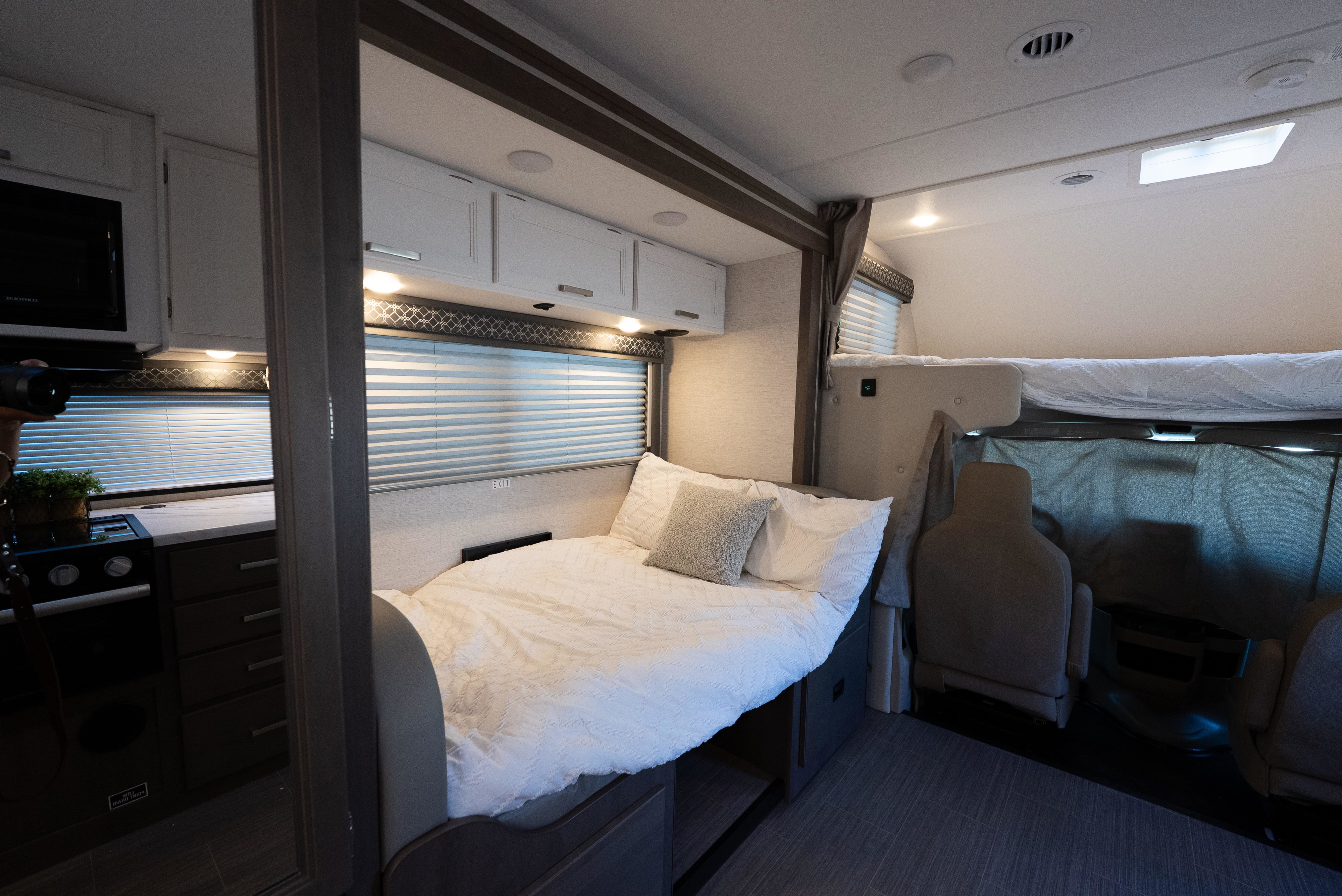 Cozy RV rental interior featuring a compact kitchenette, comfortable main bed, and an overhead bunk. Ideal for road trips!. Thor Freedom Elite 2025